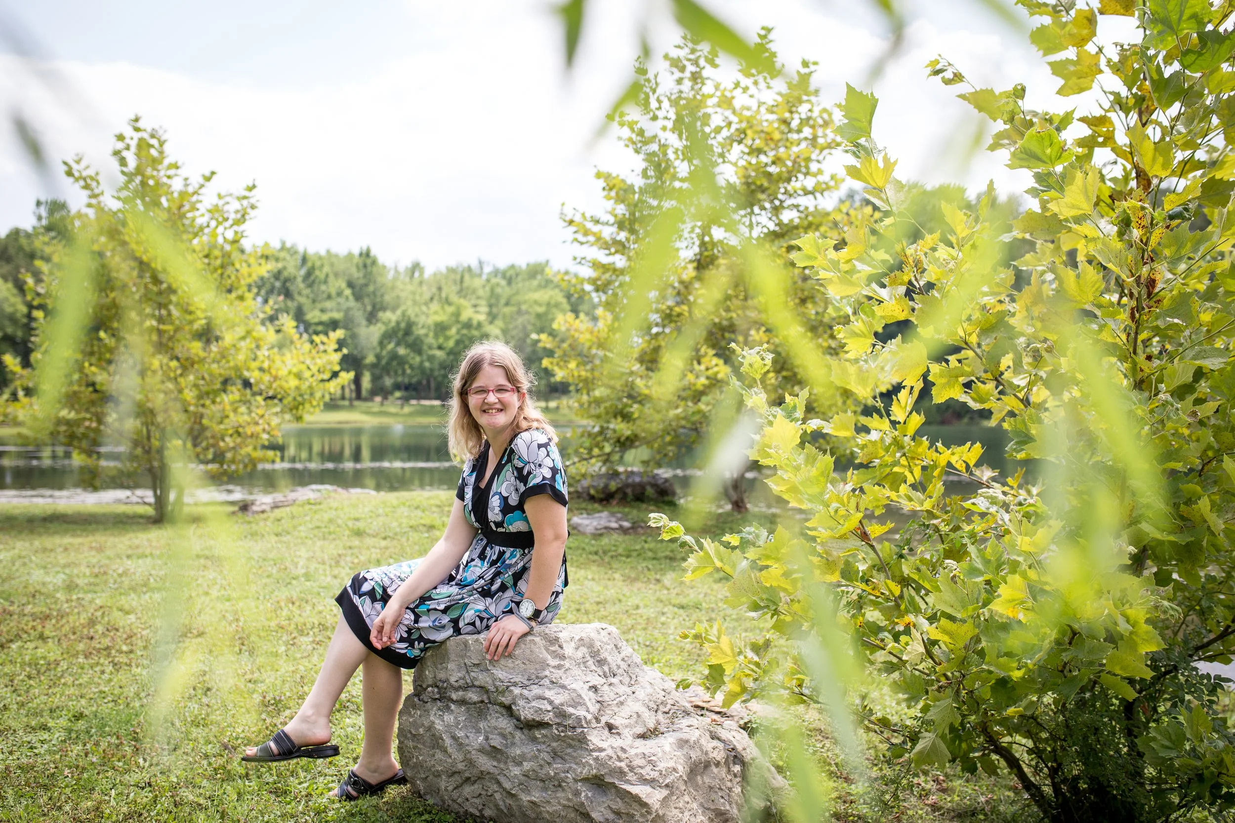young woman with disability sitting on a rock at the park smiling at camera