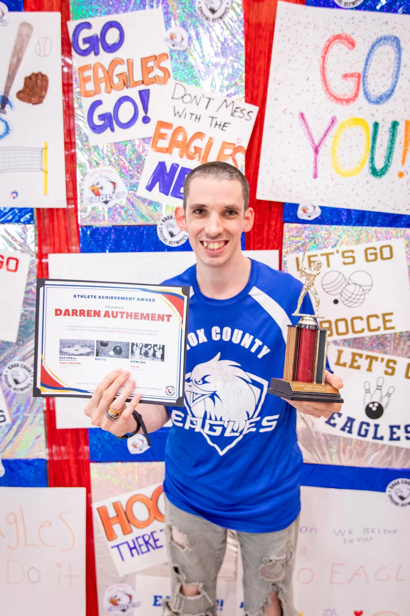 portrait of a person standing in front of a special olympics back drop, holding their trophy and certificate
