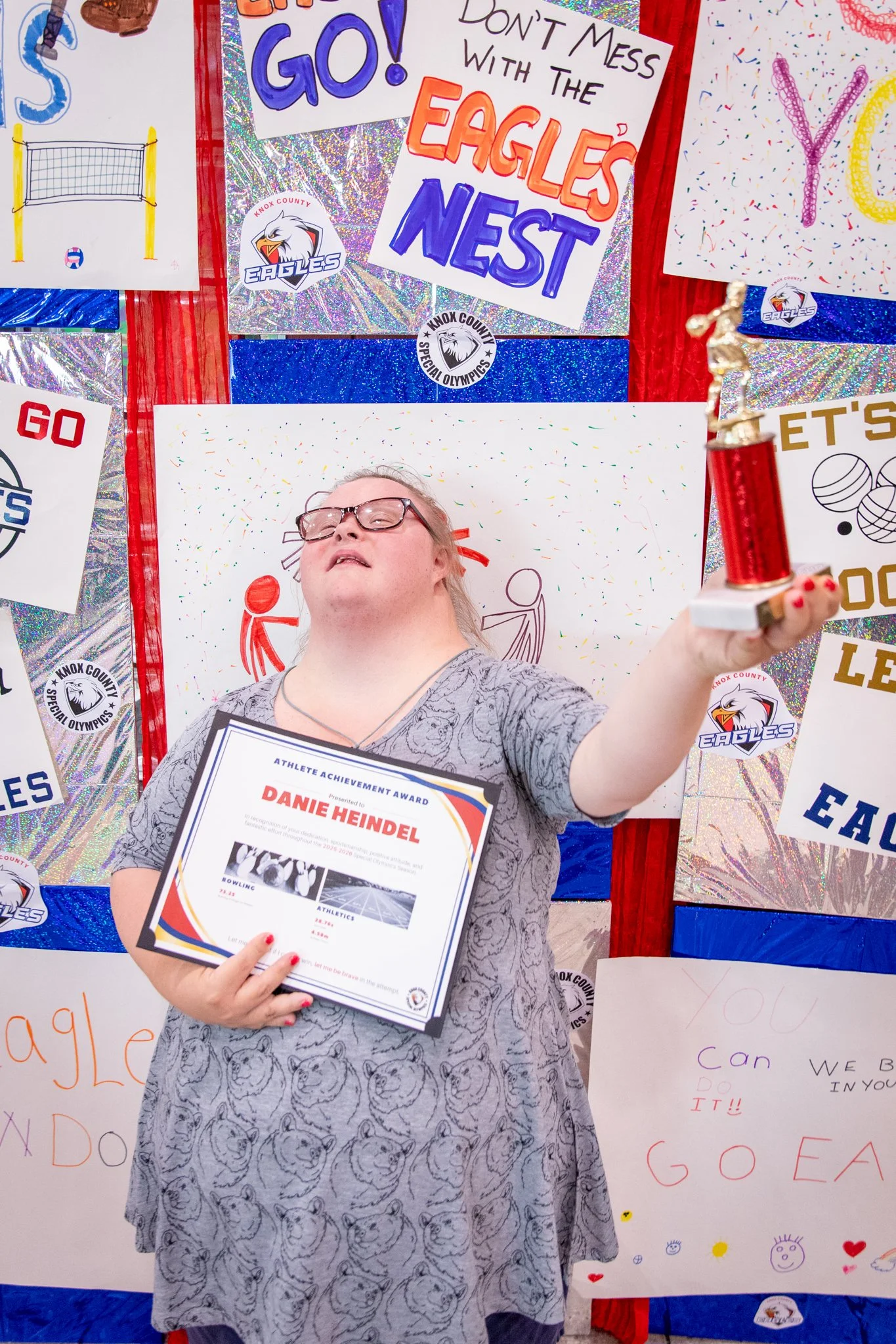 portrait of a person standing in front of a special olympics back drop, holding their trophy and certificate