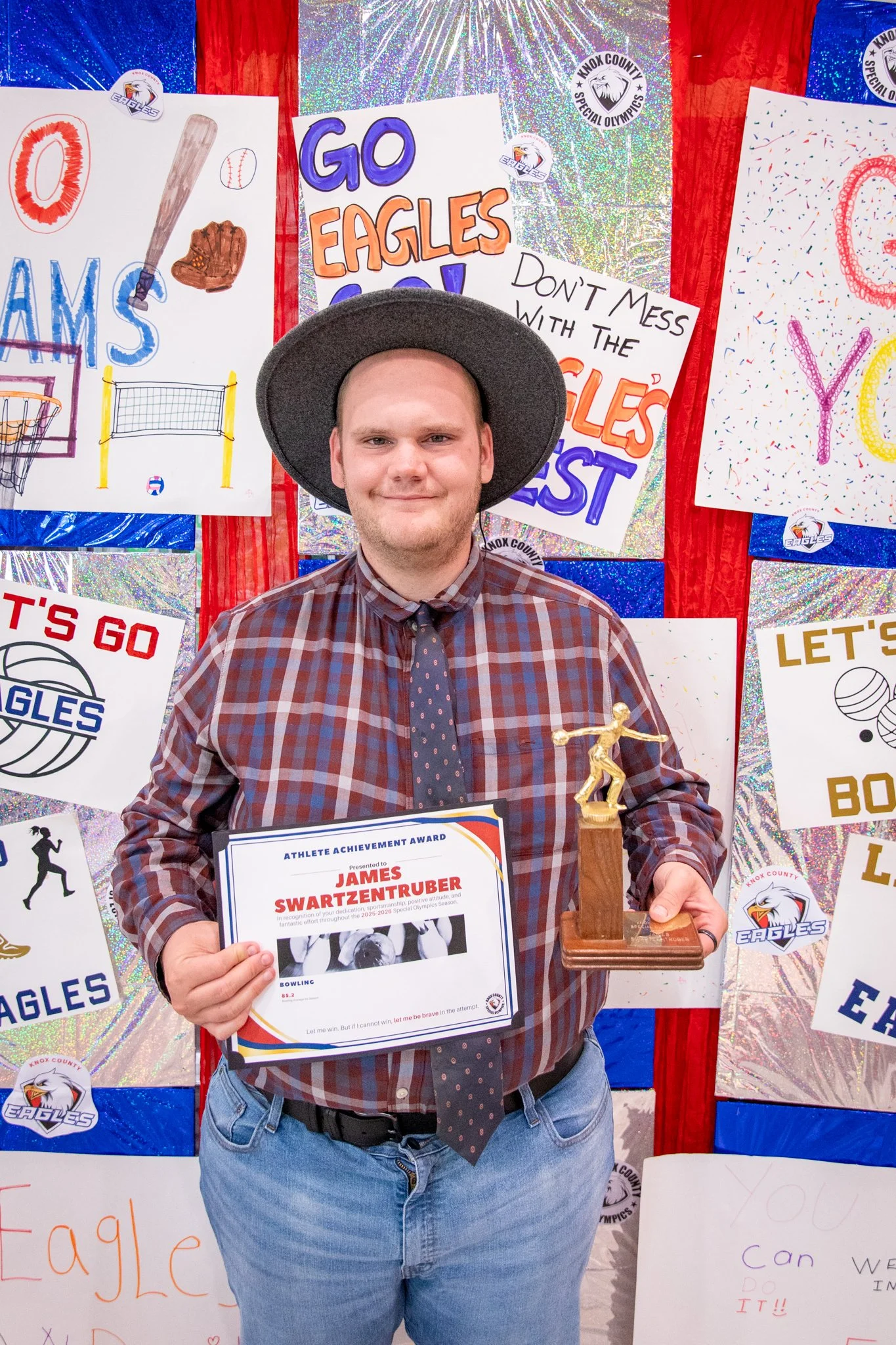 portrait of a person standing in front of a special olympics back drop, holding their trophy and certificate