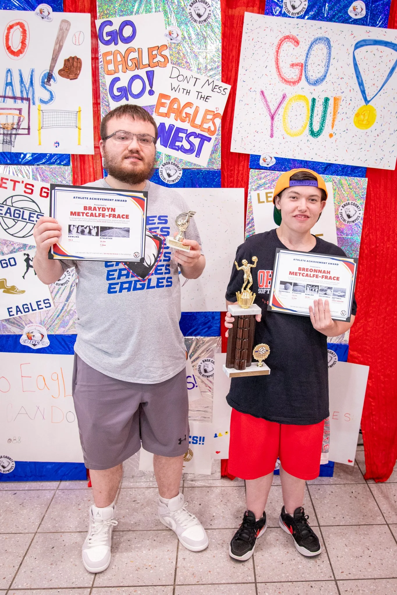 portrait of a person standing in front of a special olympics back drop, holding their trophy and certificate