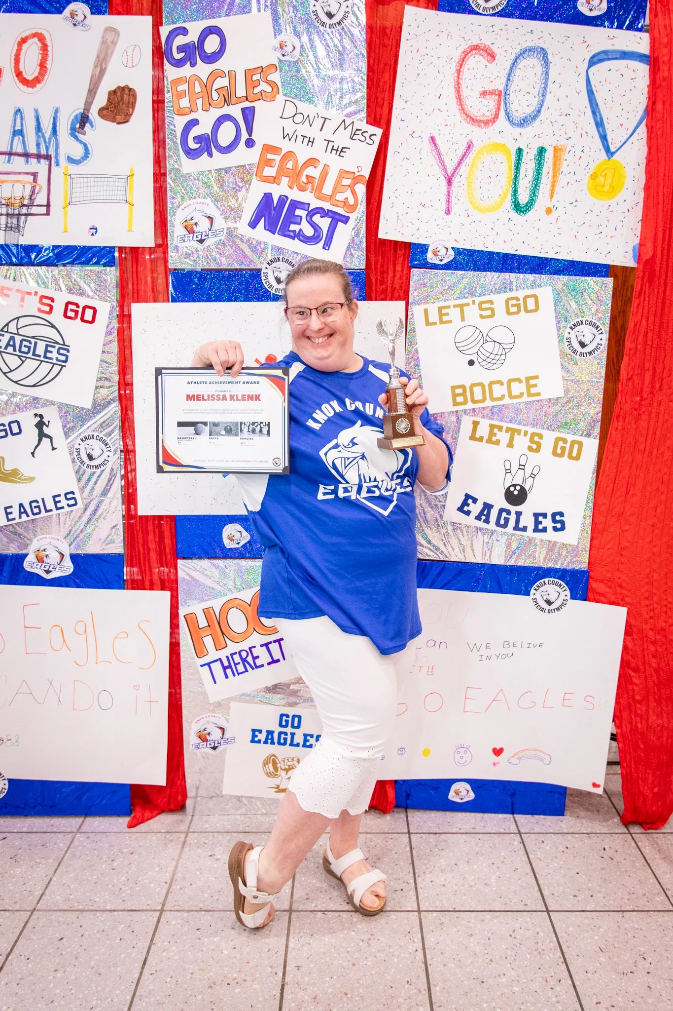 portrait of a person standing in front of a special olympics back drop, holding their trophy and certificate