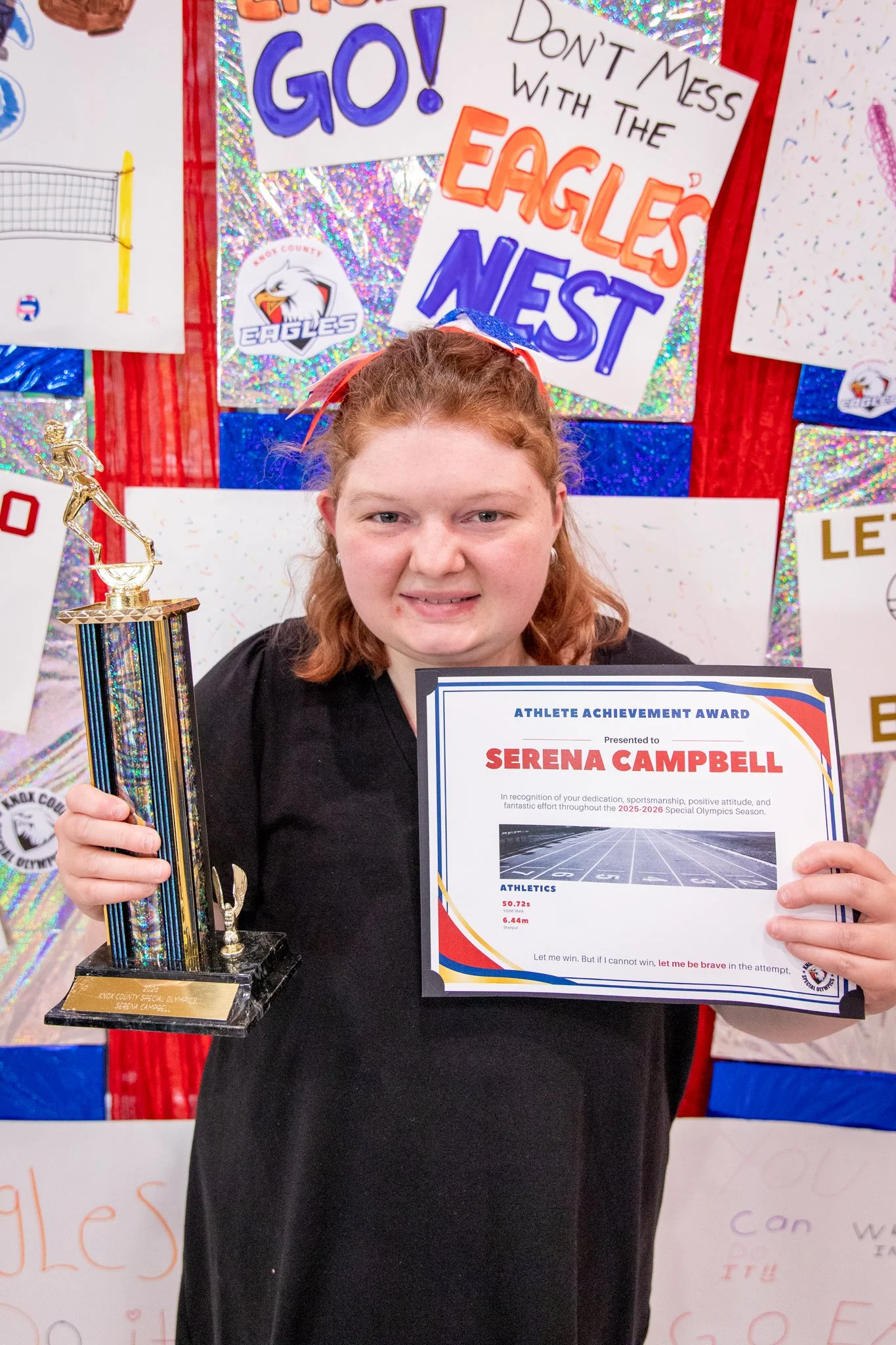 portrait of a person standing in front of a special olympics back drop, holding their trophy and certificate