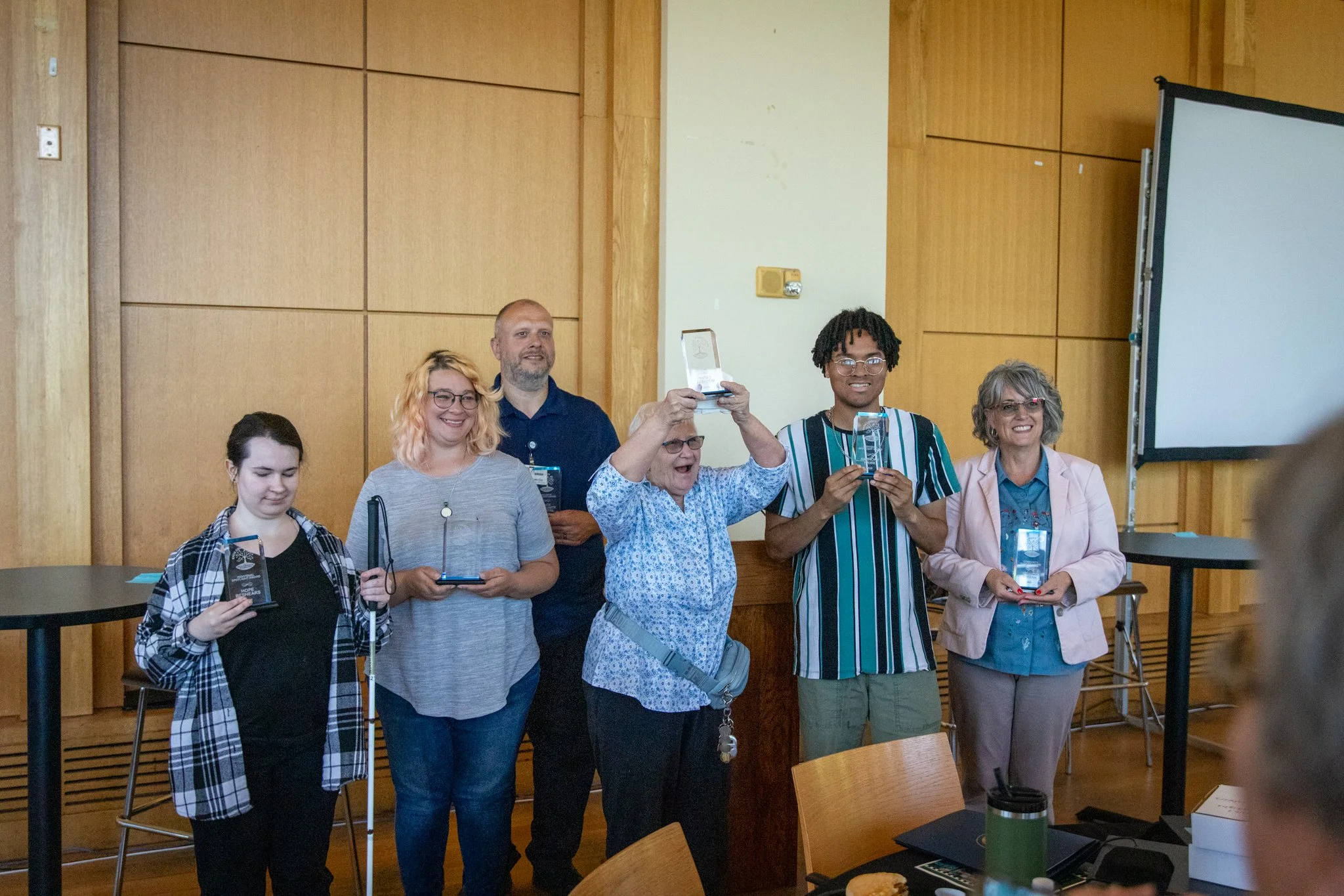 group of 6 people standing in a row, each holding a glass award.  they are smiling at the camera.