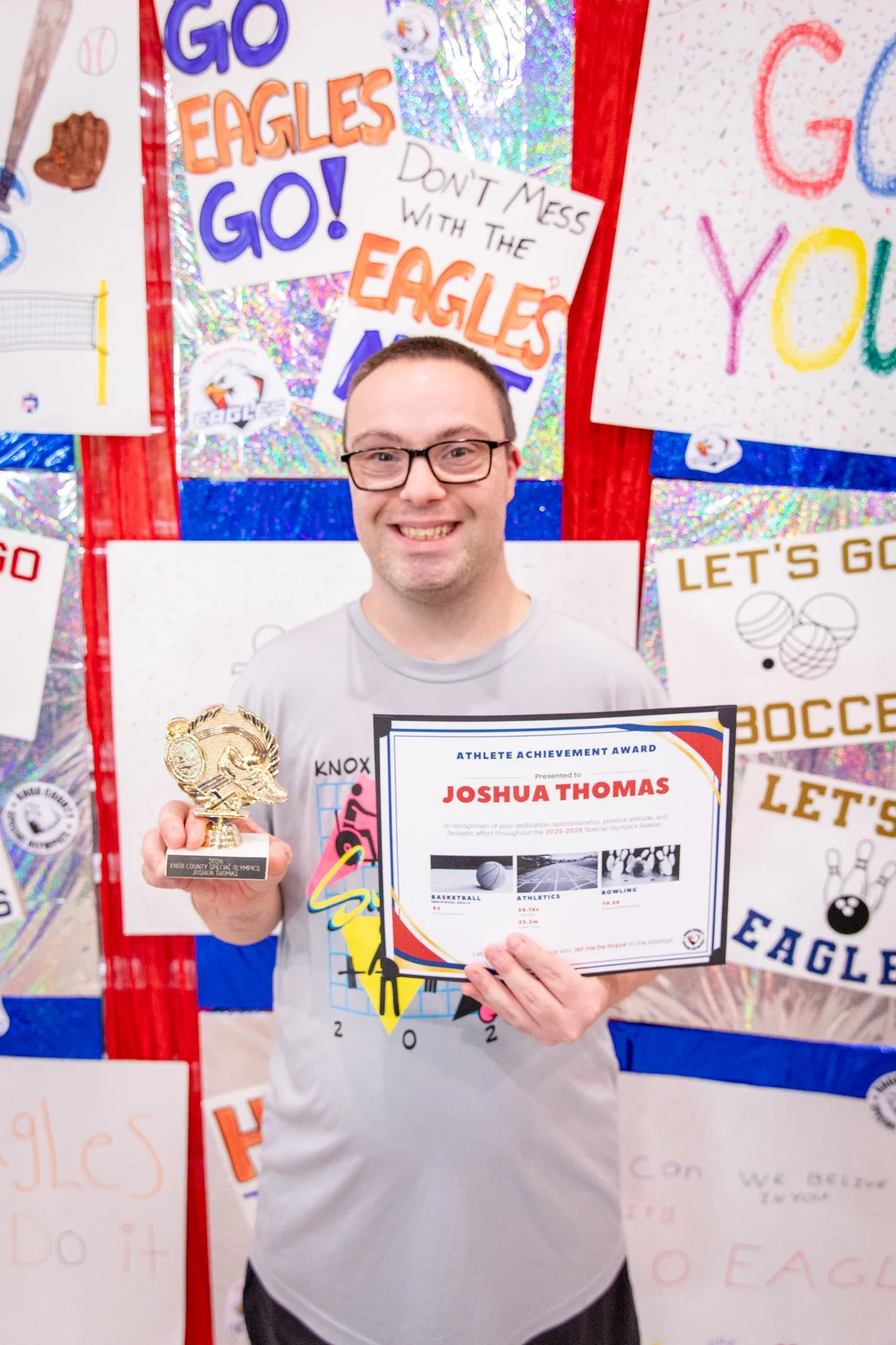 portrait of a person standing in front of a special olympics back drop, holding their trophy and certificate