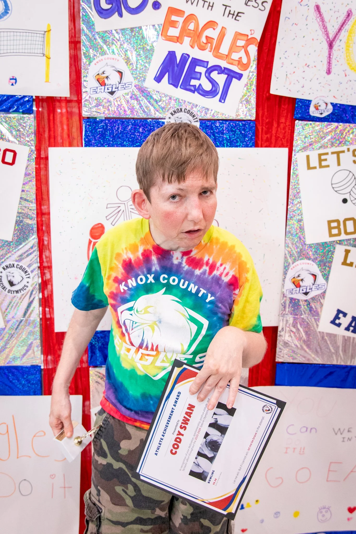 portrait of a person standing in front of a special olympics back drop, holding their trophy and certificate