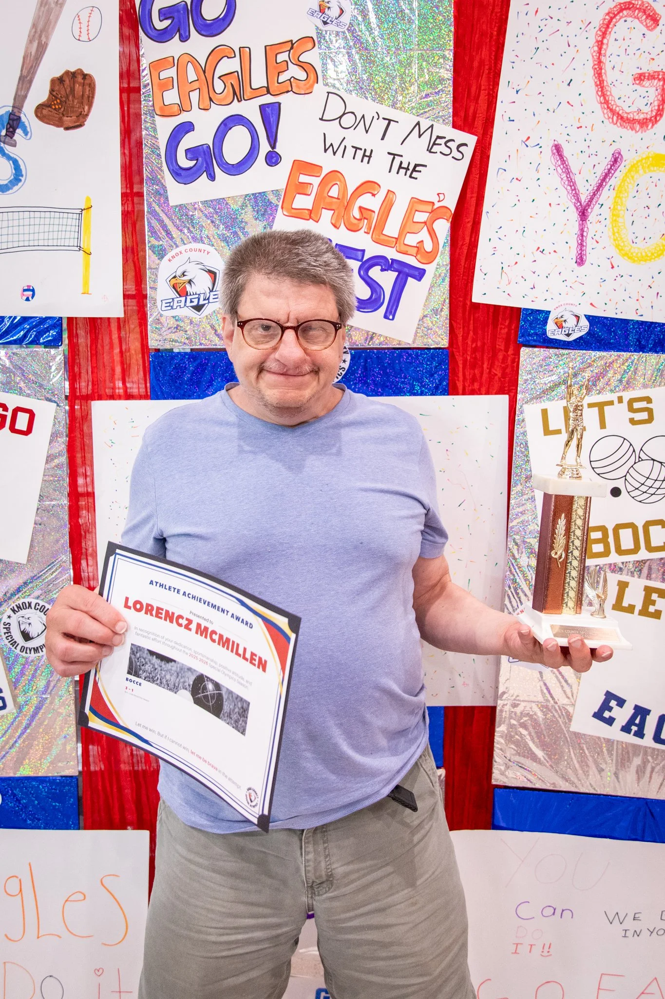 portrait of a person standing in front of a special olympics back drop, holding their trophy and certificate