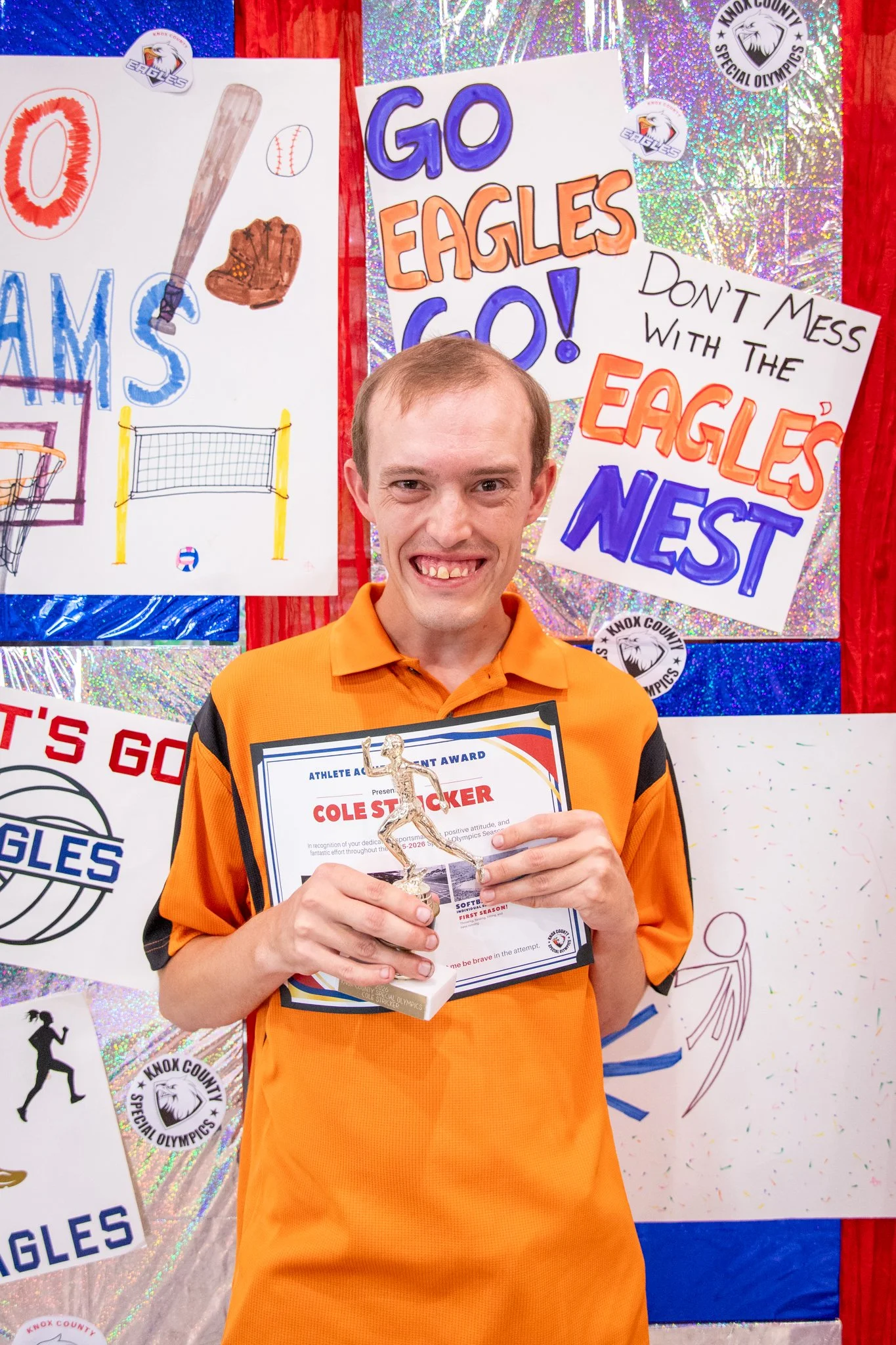 portrait of a person standing in front of a special olympics back drop, holding their trophy and certificate