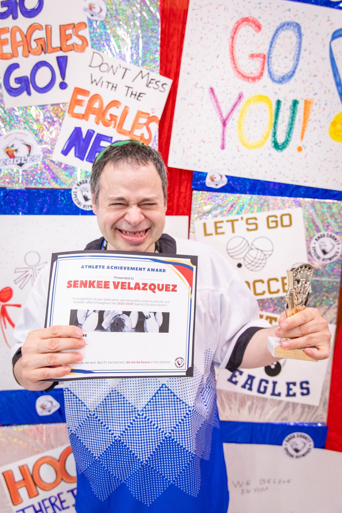 portrait of a person standing in front of a special olympics back drop, holding their trophy and certificate