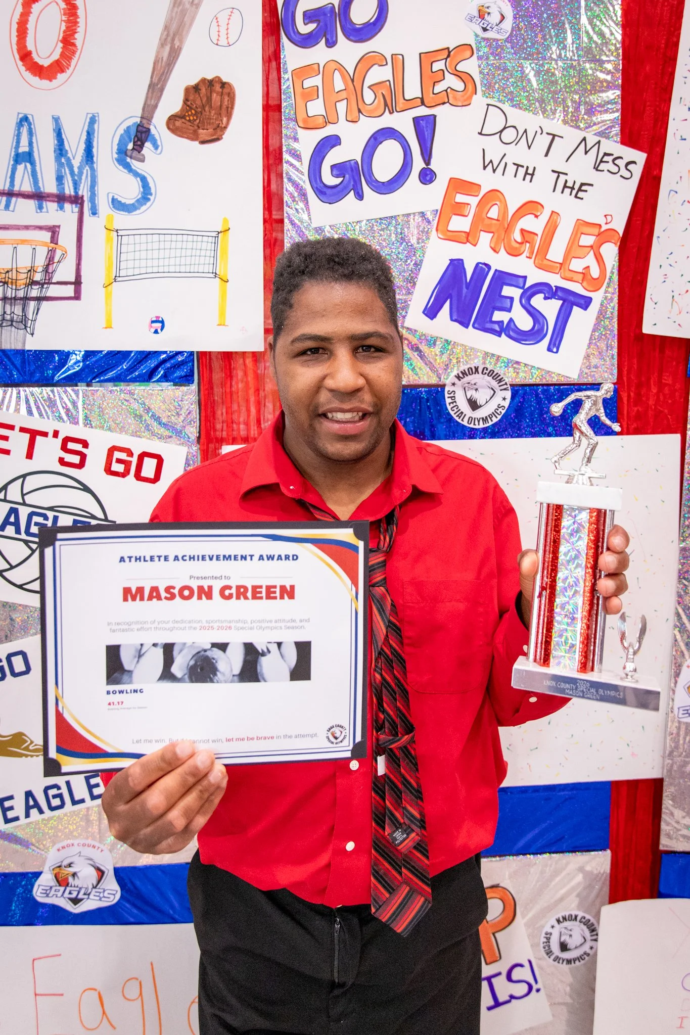 portrait of a person standing in front of a special olympics back drop, holding their trophy and certificate