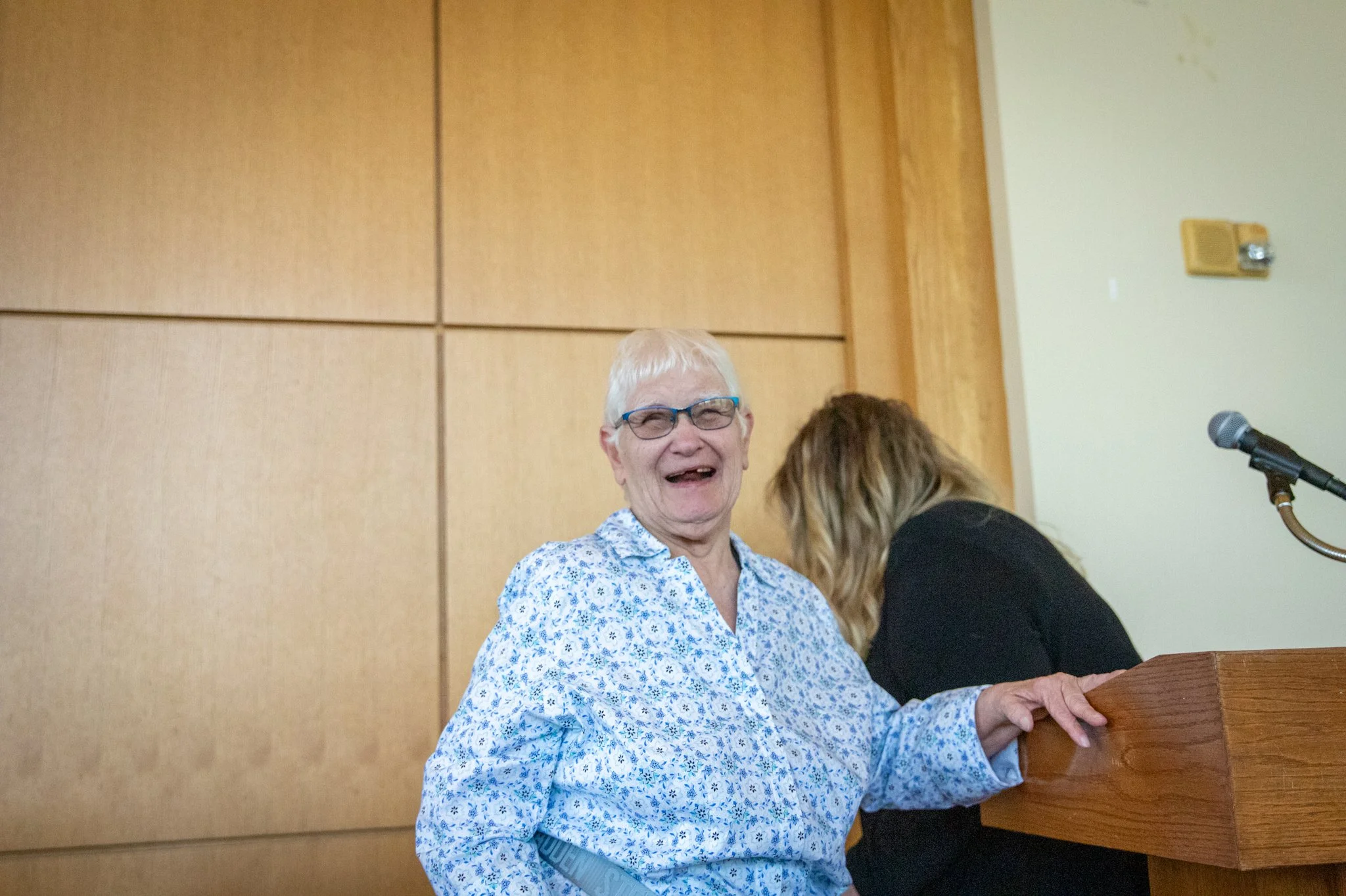 Elderly woman stands next to a wooden podium smiling
