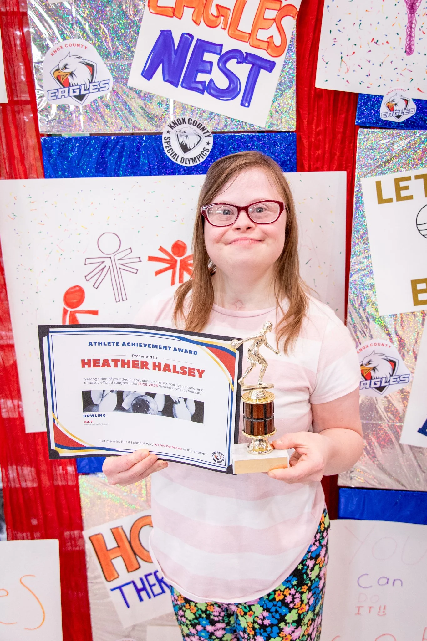 portrait of a person standing in front of a special olympics back drop, holding their trophy and certificate