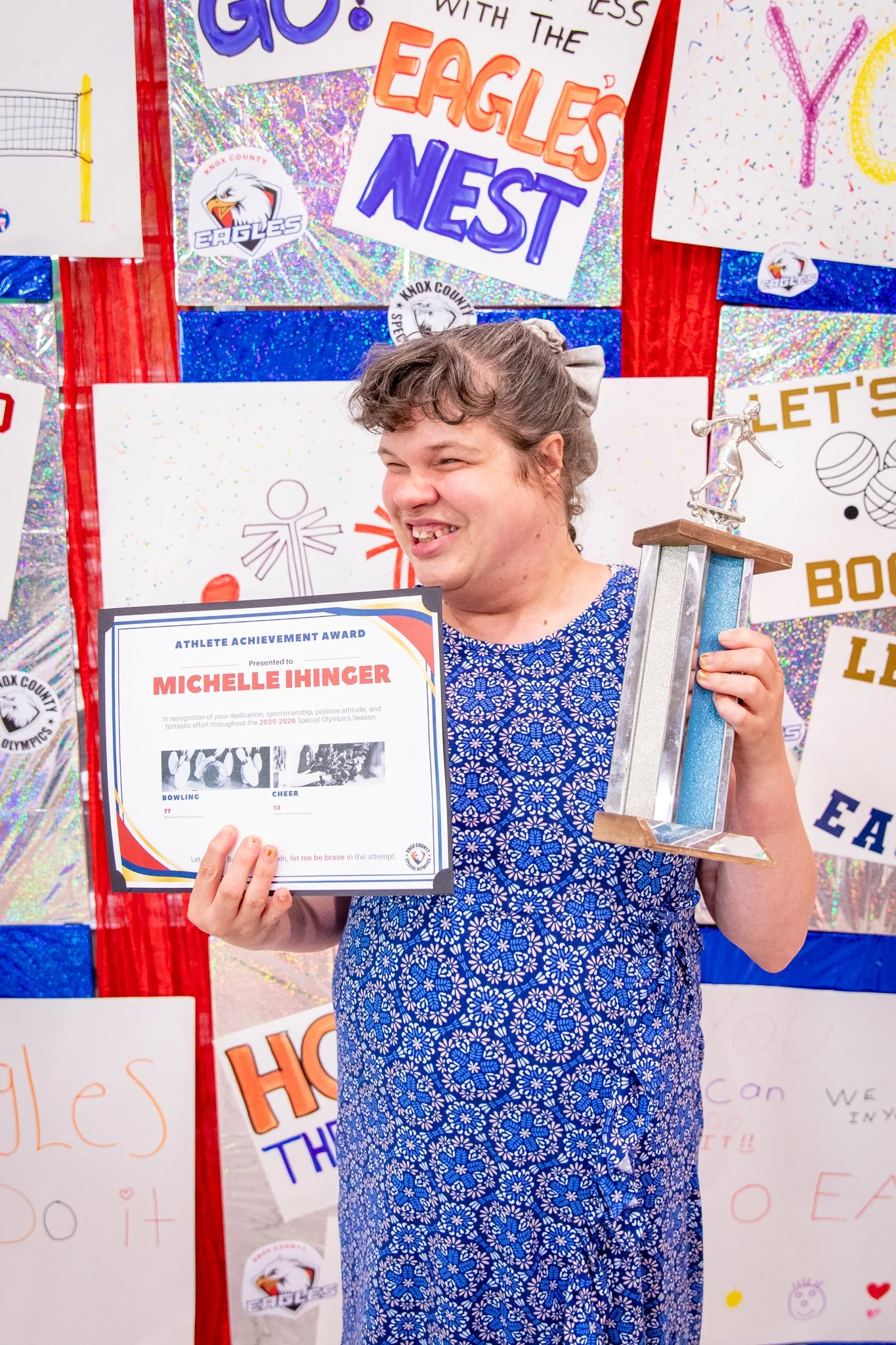 portrait of a person standing in front of a special olympics back drop, holding their trophy and certificate