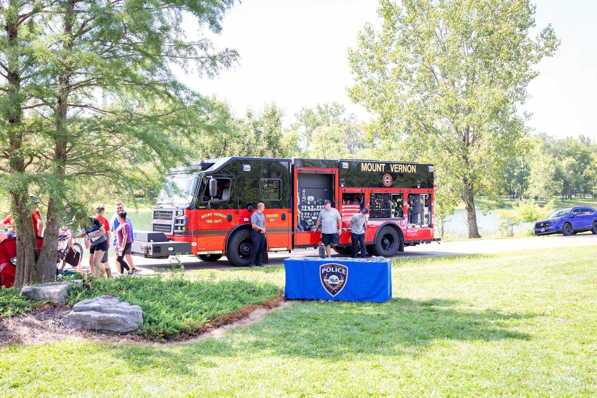 orange and black fire truck in the distance.  surrounded by trees and a pond