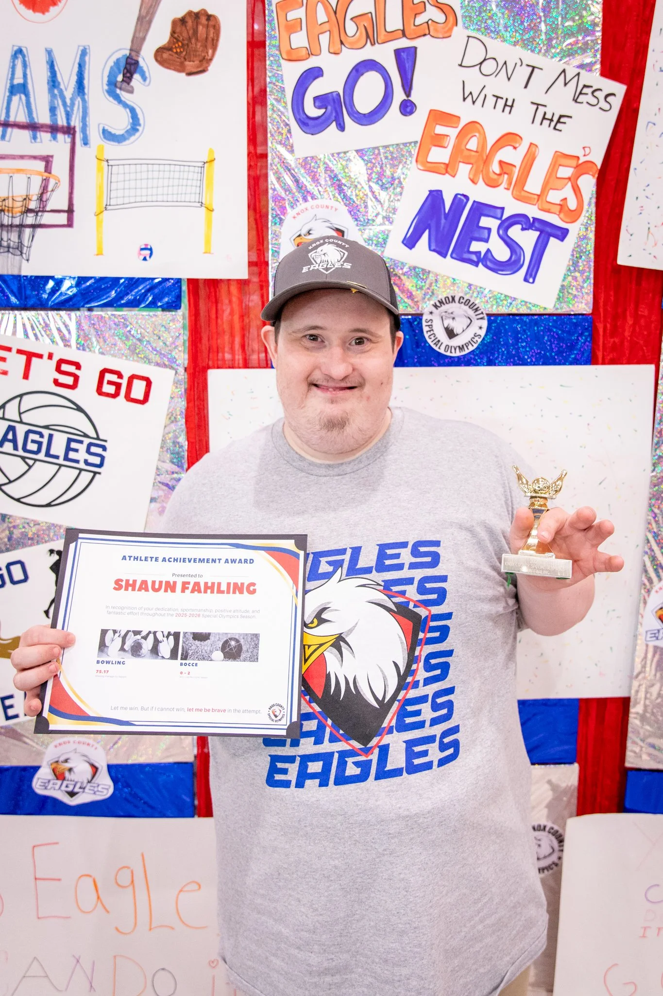 portrait of a person standing in front of a special olympics back drop, holding their trophy and certificate
