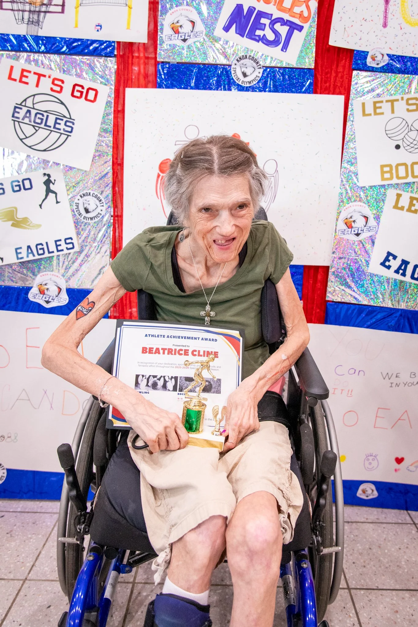 portrait of a person standing in front of a special olympics back drop, holding their trophy and certificate
