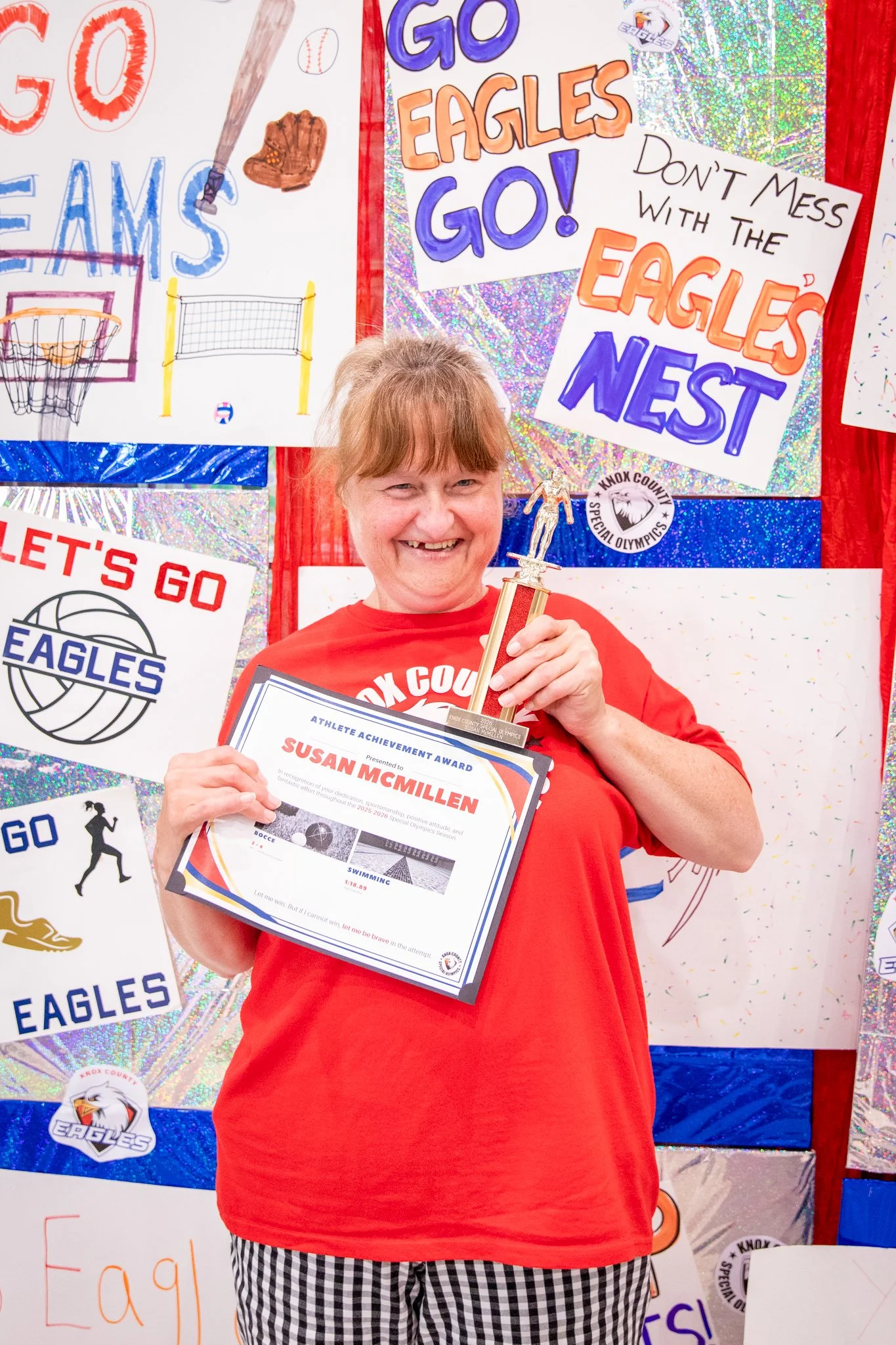 portrait of a person standing in front of a special olympics back drop, holding their trophy and certificate