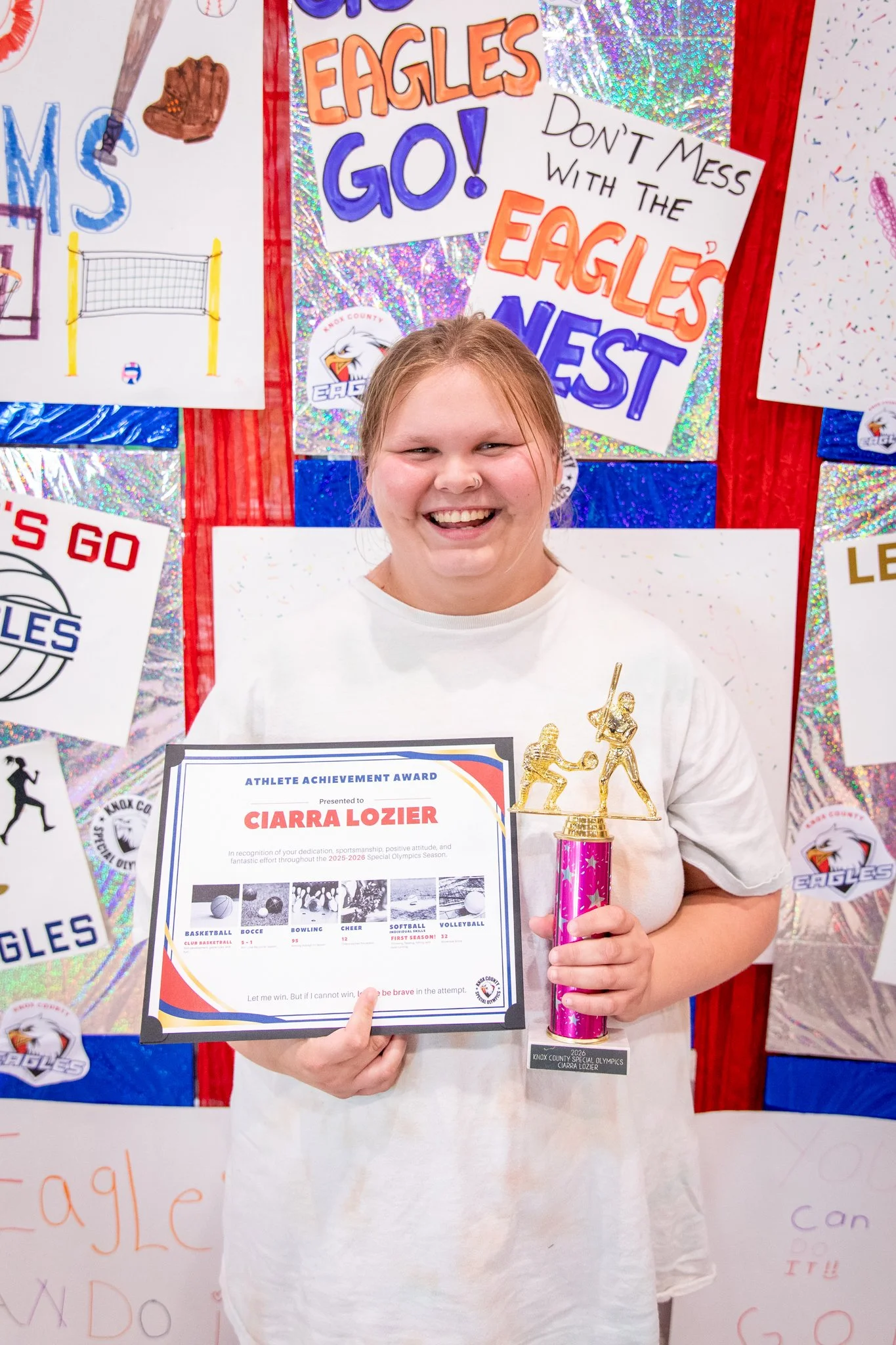 portrait of a person standing in front of a special olympics back drop, holding their trophy and certificate