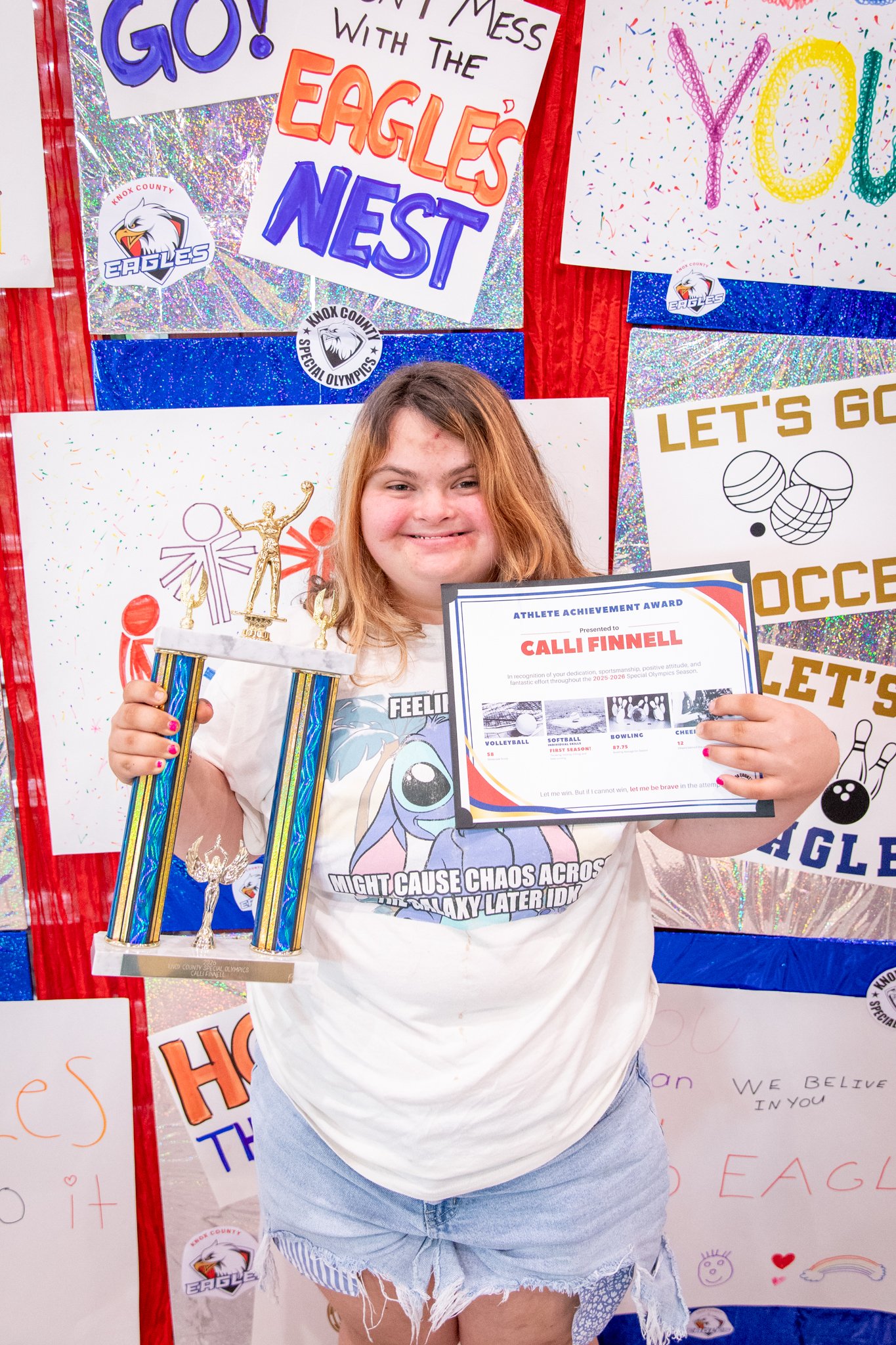 portrait of a person standing in front of a special olympics back drop, holding their trophy and certificate