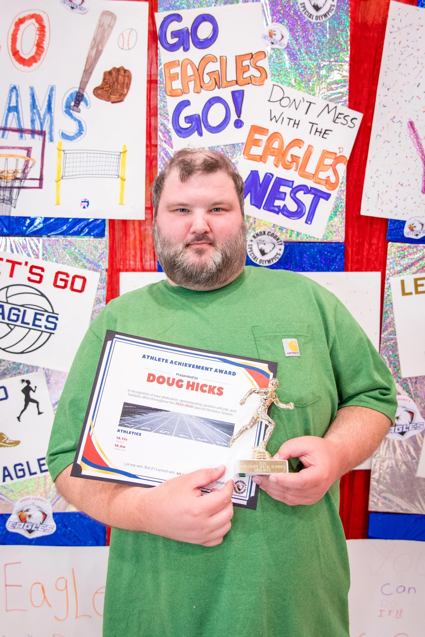 portrait of a person standing in front of a special olympics back drop, holding their trophy and certificate