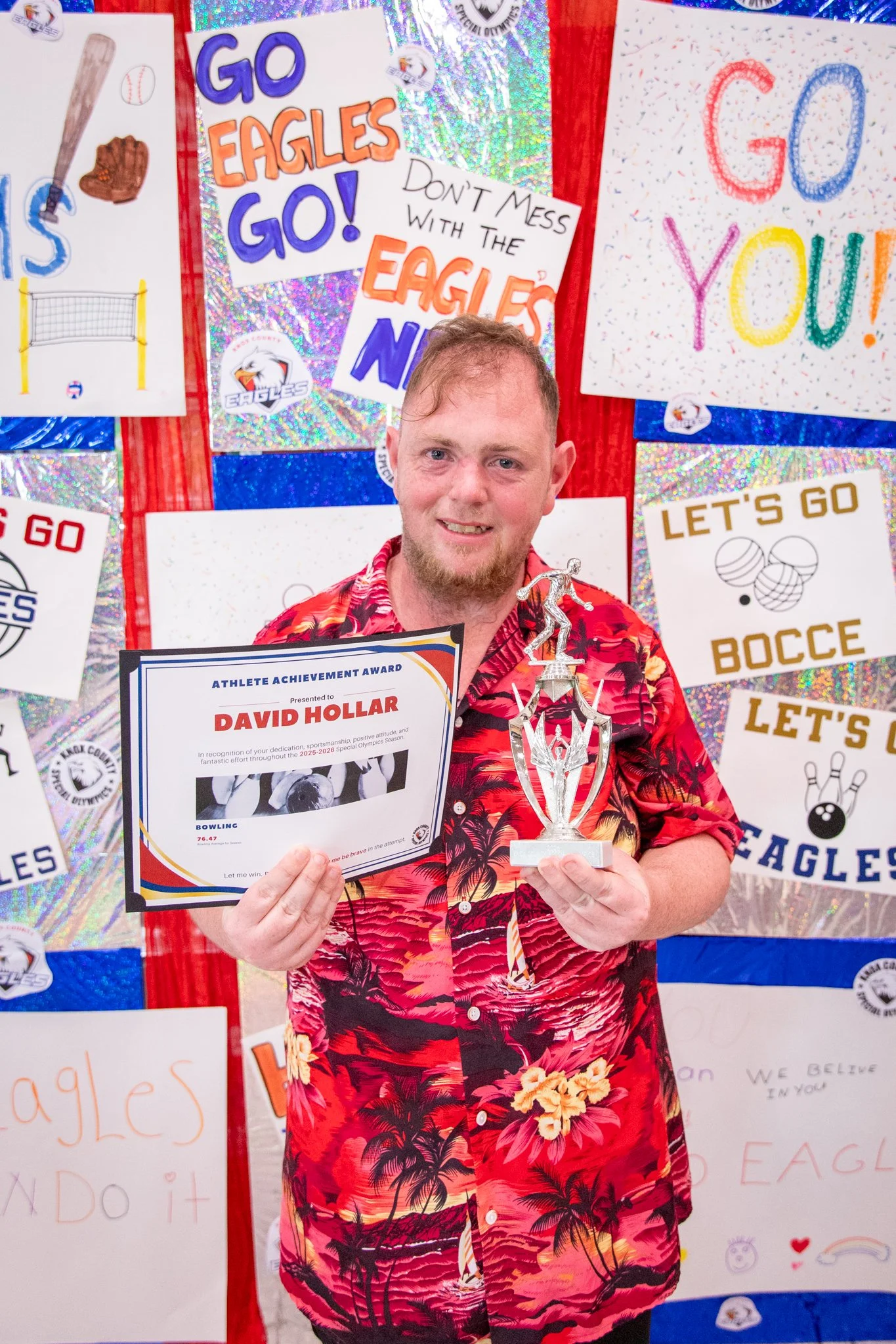 portrait of a person standing in front of a special olympics back drop, holding their trophy and certificate