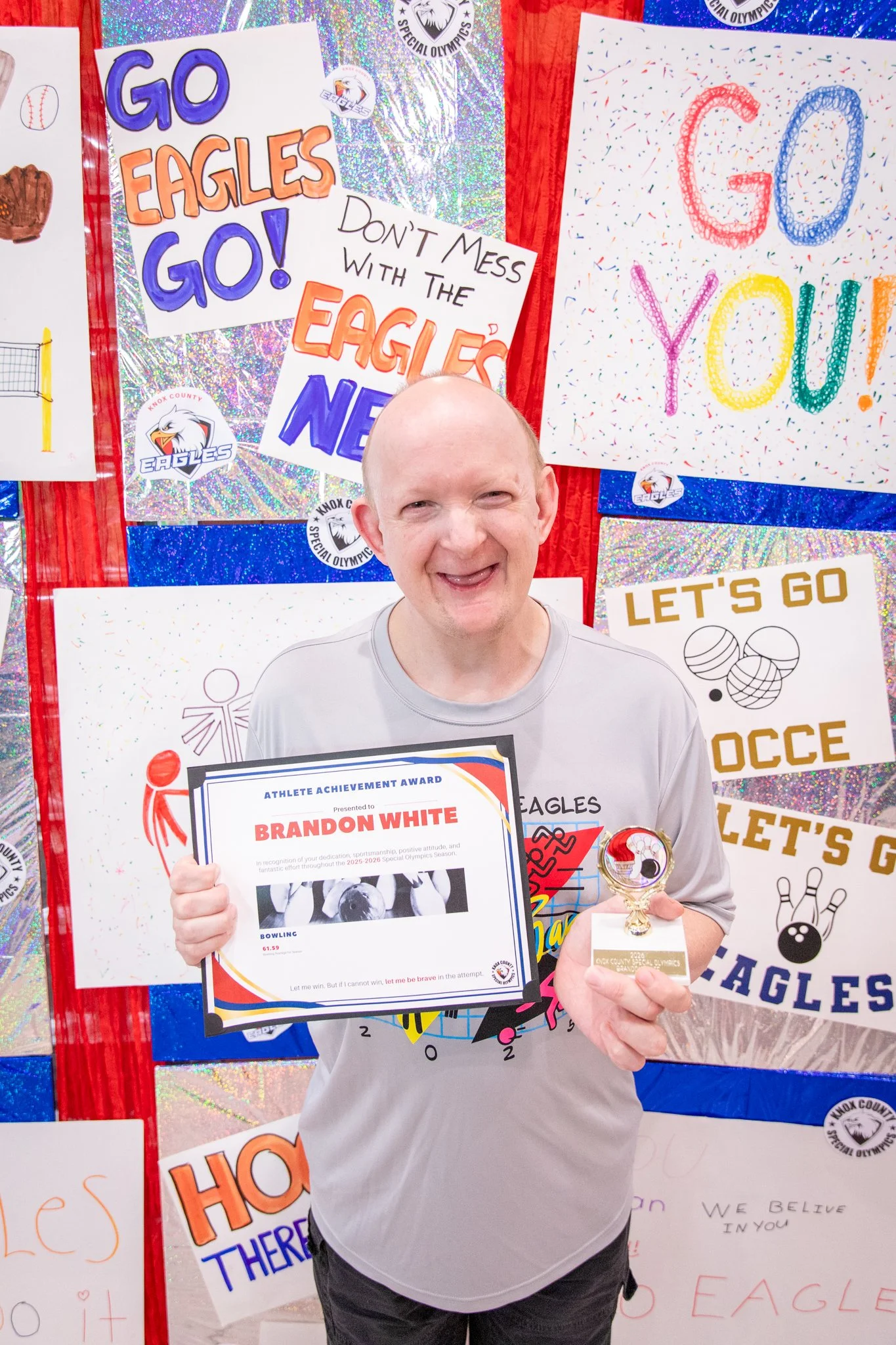 portrait of a person standing in front of a special olympics back drop, holding their trophy and certificate