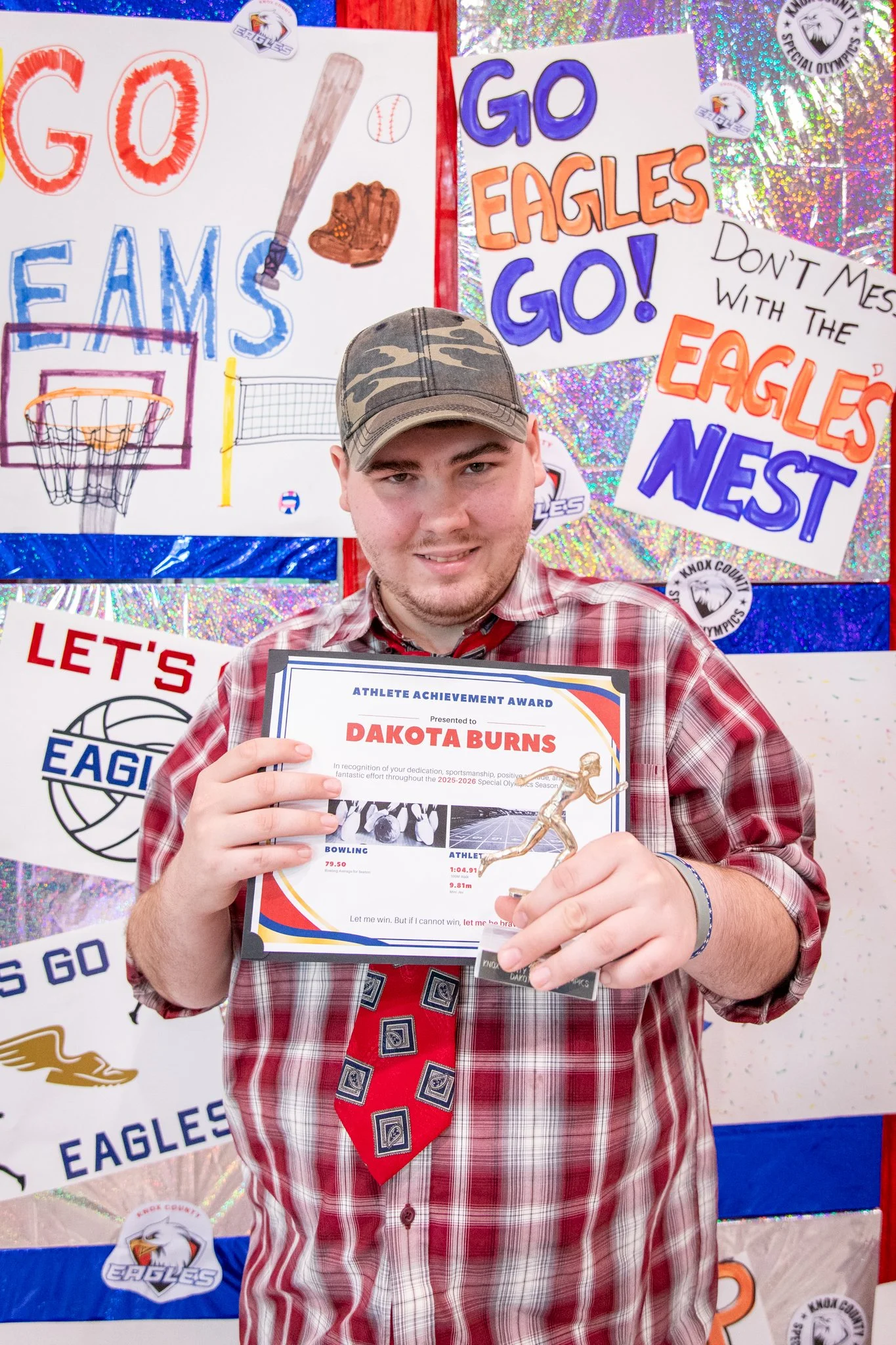 portrait of a person standing in front of a special olympics back drop, holding their trophy and certificate