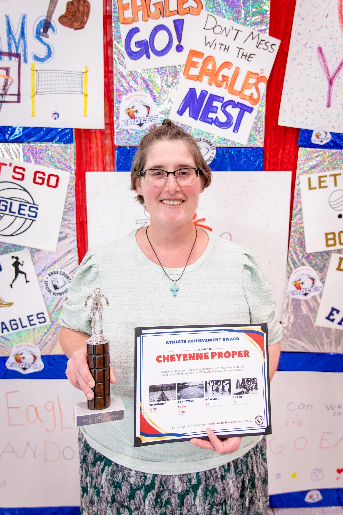 portrait of a person standing in front of a special olympics back drop, holding their trophy and certificate