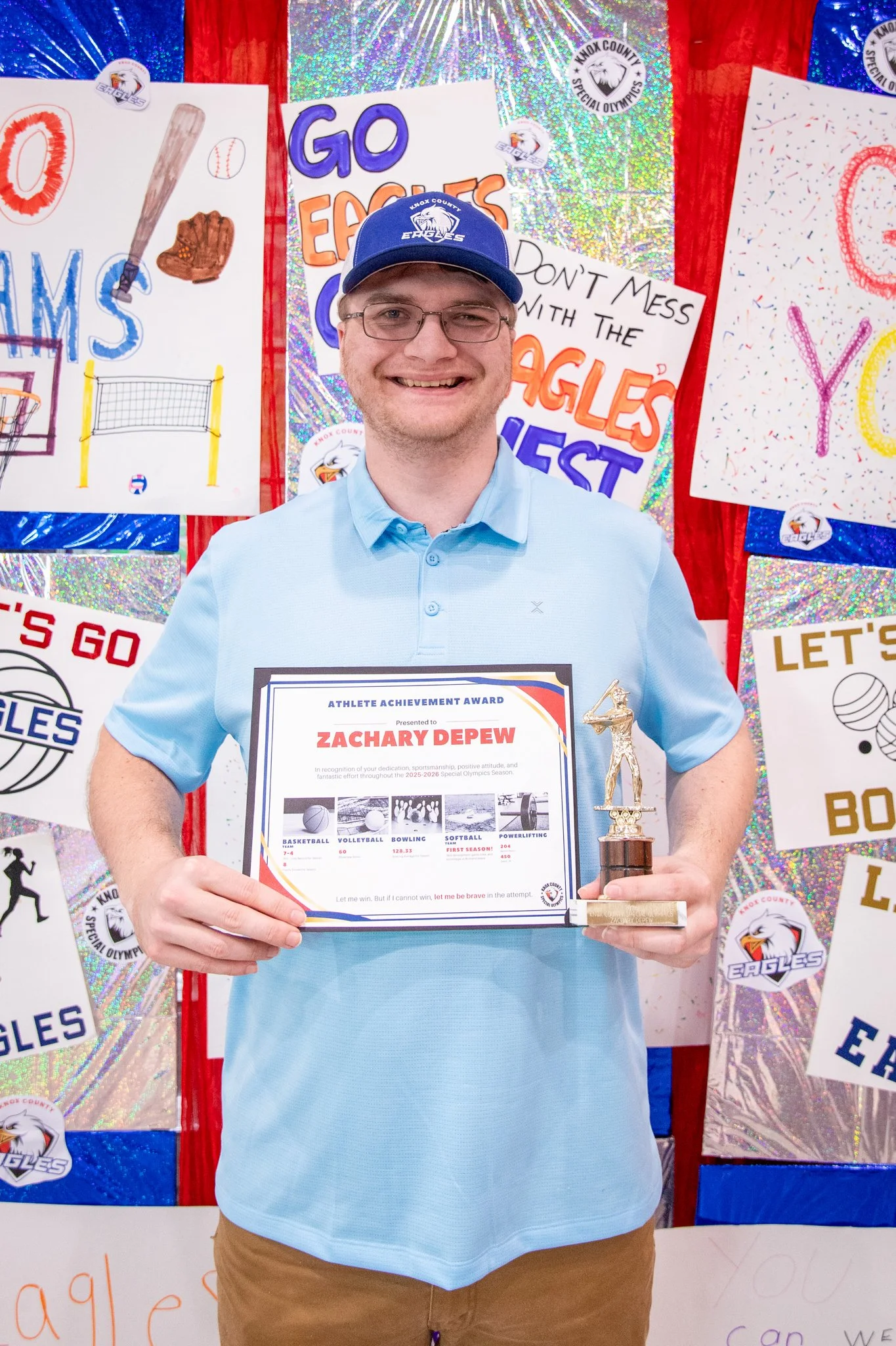portrait of a person standing in front of a special olympics back drop, holding their trophy and certificate