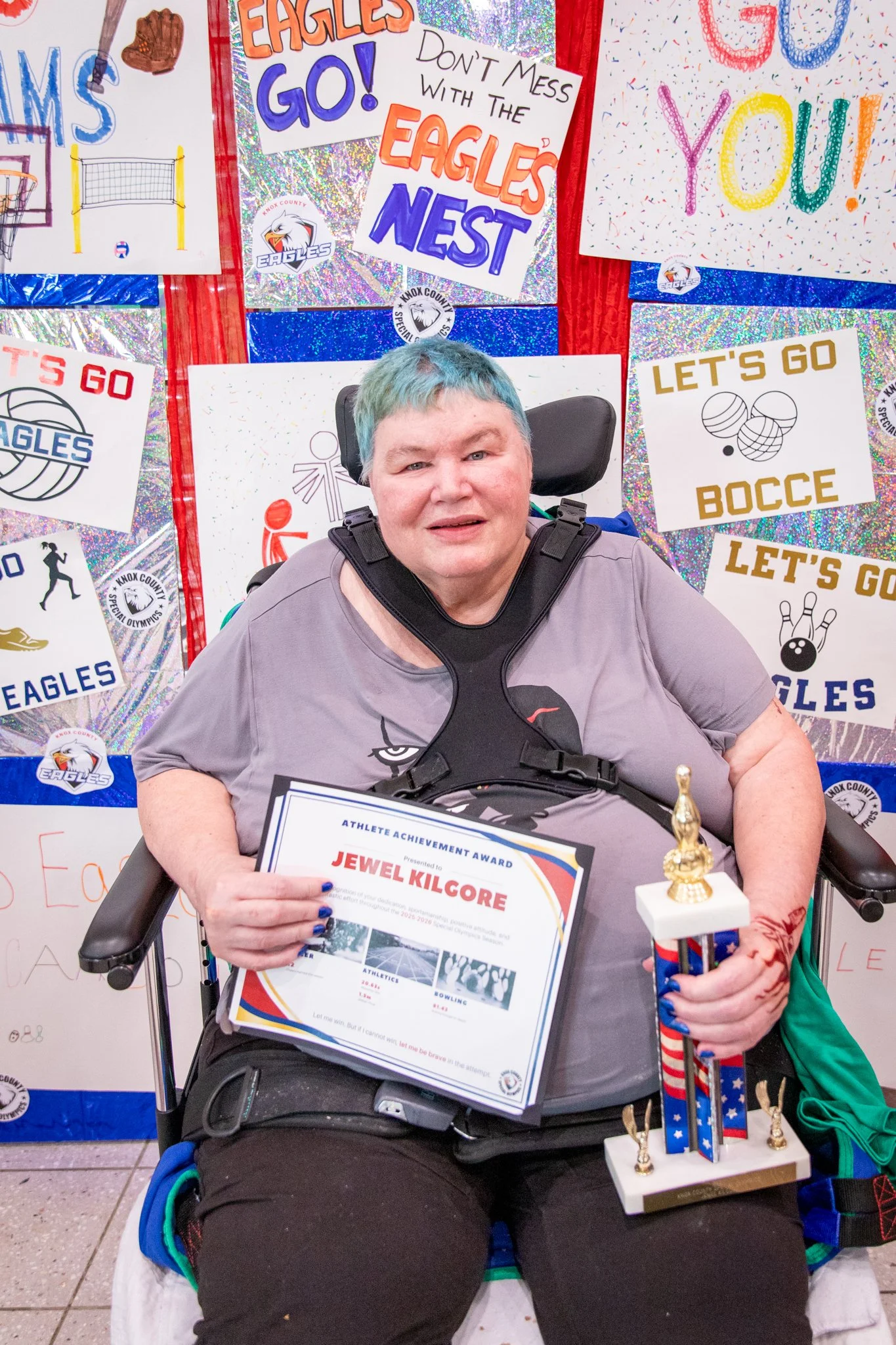 portrait of a person standing in front of a special olympics back drop, holding their trophy and certificate
