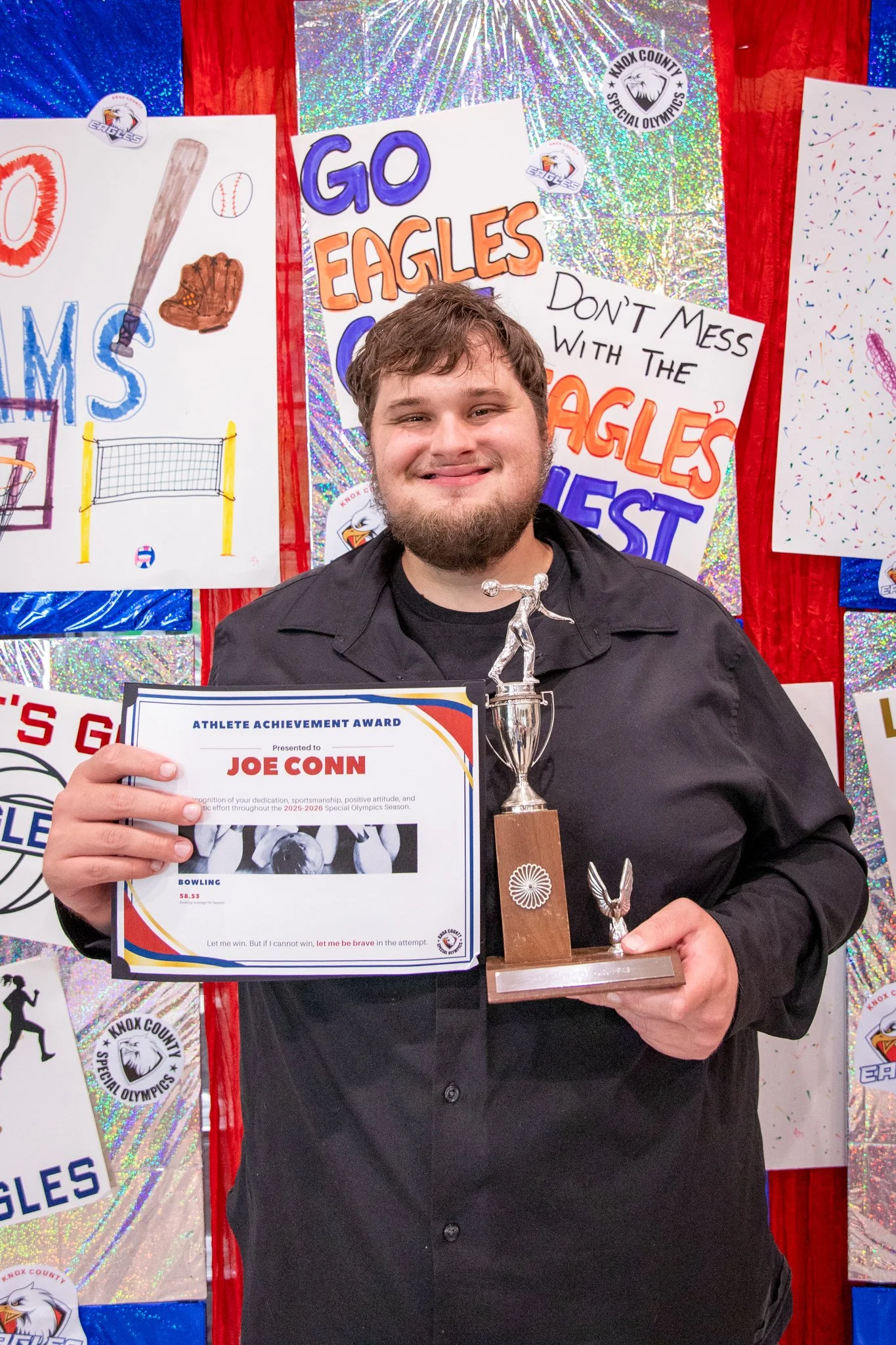 portrait of a person standing in front of a special olympics back drop, holding their trophy and certificate