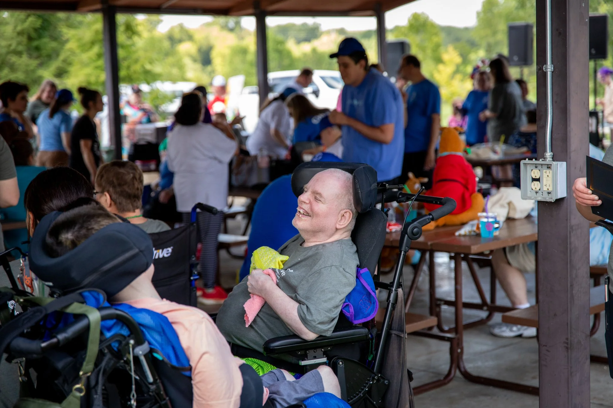 man in a wheelchair smiling brightly.  People are in the background at an event.