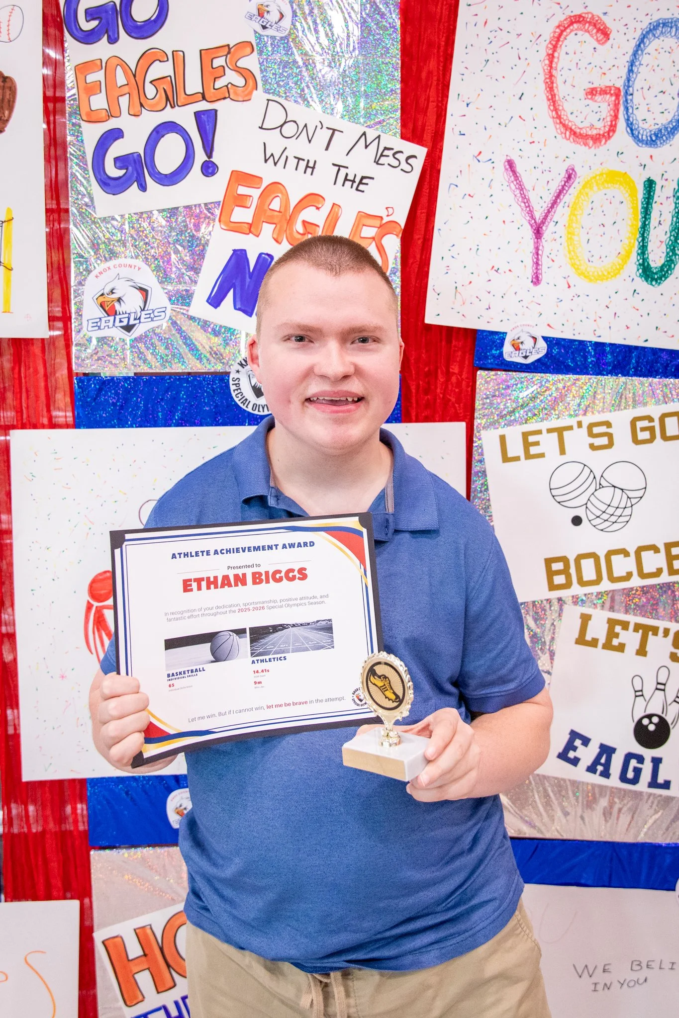 portrait of a person standing in front of a special olympics back drop, holding their trophy and certificate