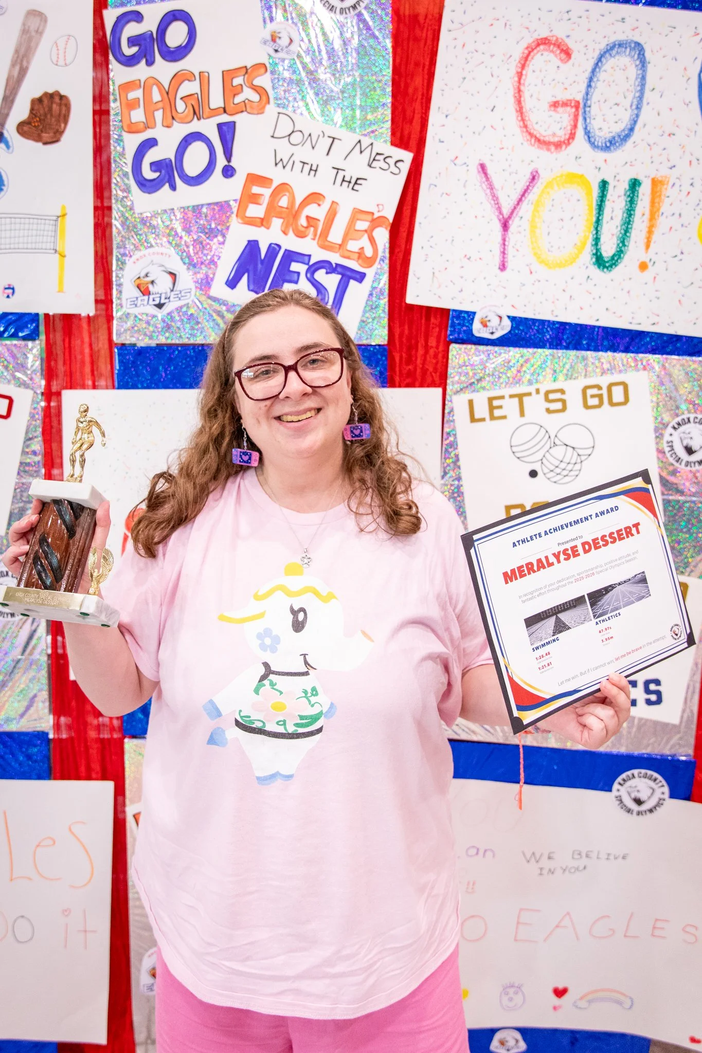 portrait of a person standing in front of a special olympics back drop, holding their trophy and certificate