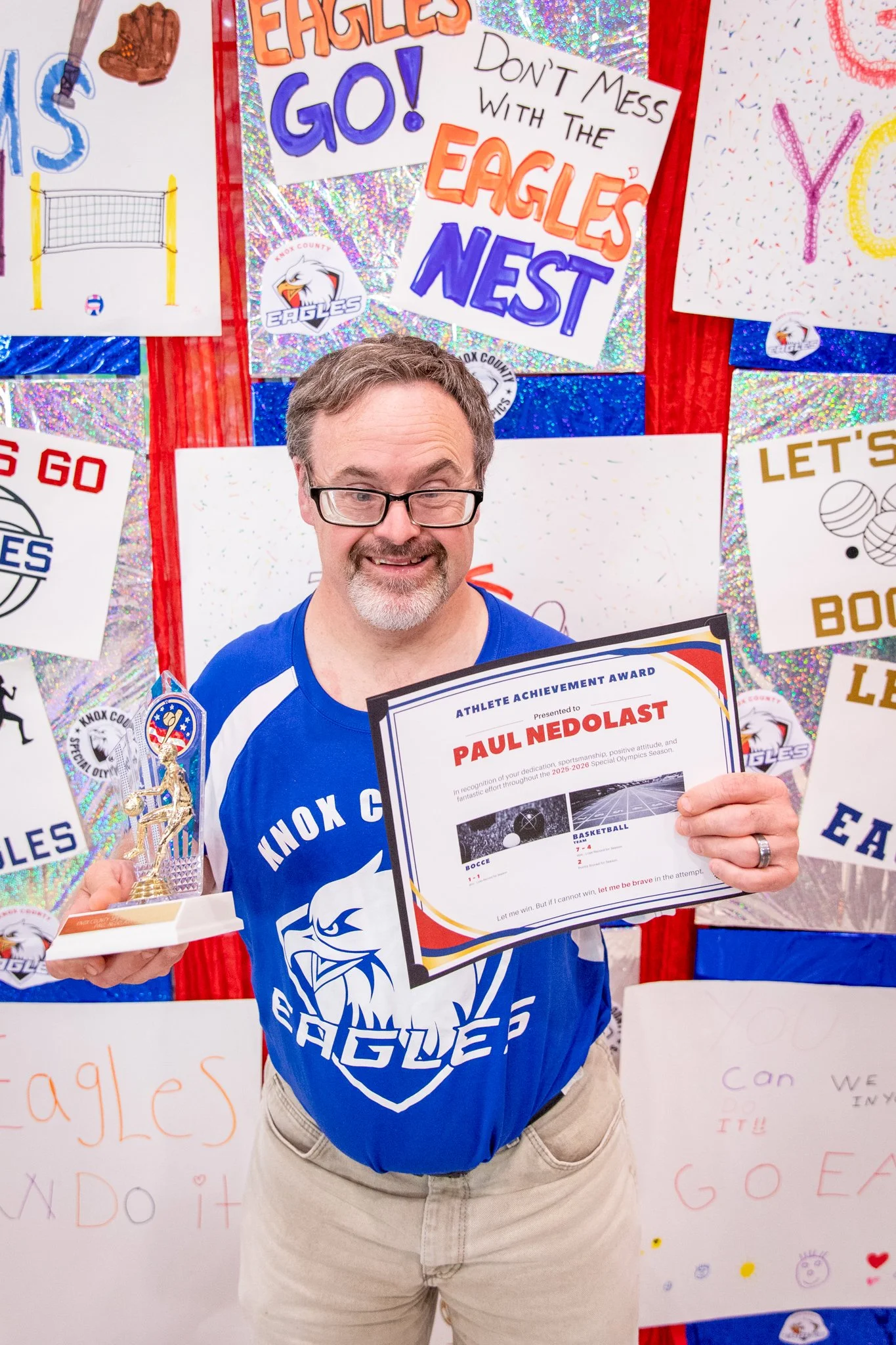 portrait of a person standing in front of a special olympics back drop, holding their trophy and certificate