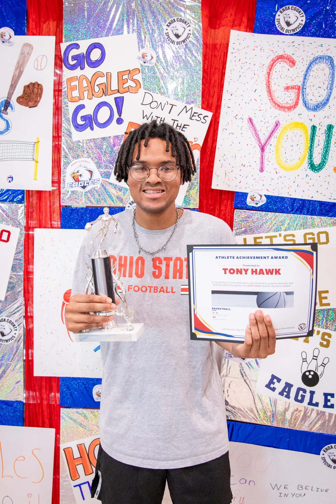 portrait of a person standing in front of a special olympics back drop, holding their trophy and certificate