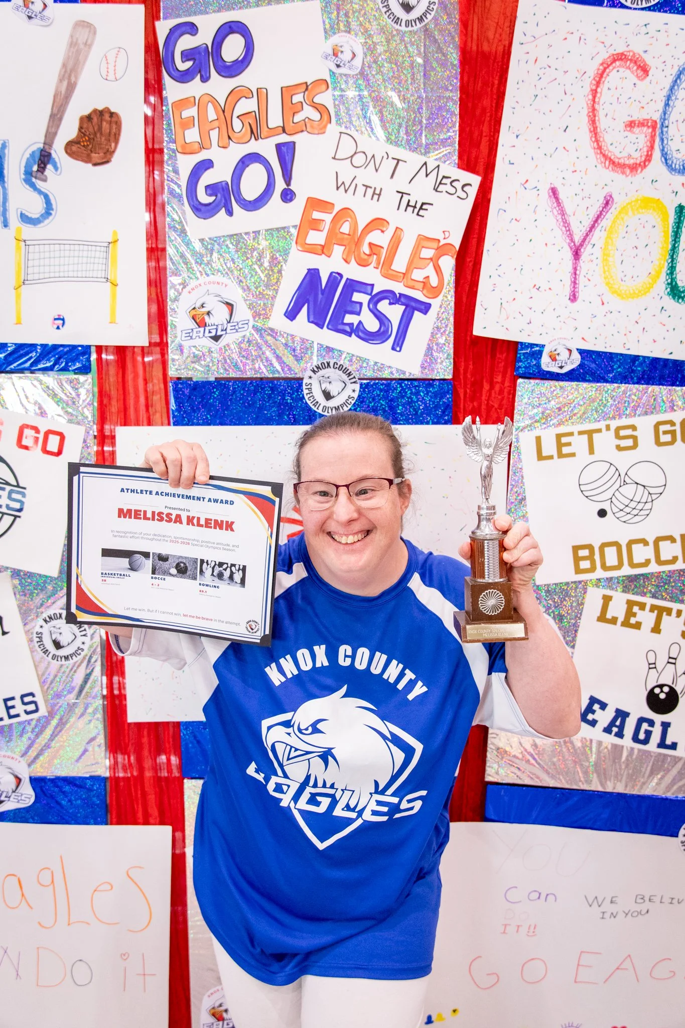 portrait of a person standing in front of a special olympics back drop, holding their trophy and certificate