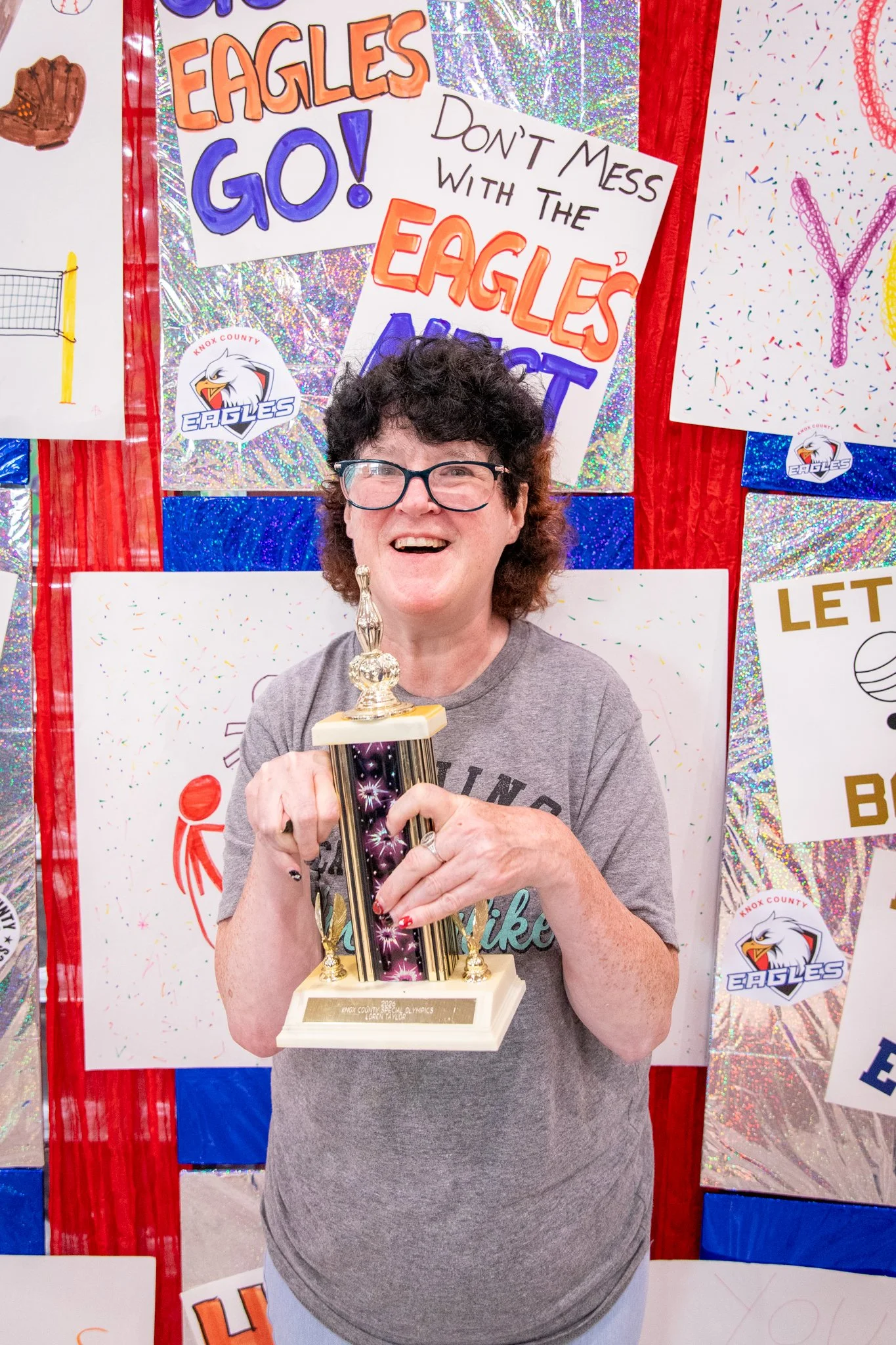 portrait of a person standing in front of a special olympics back drop, holding their trophy and certificate
