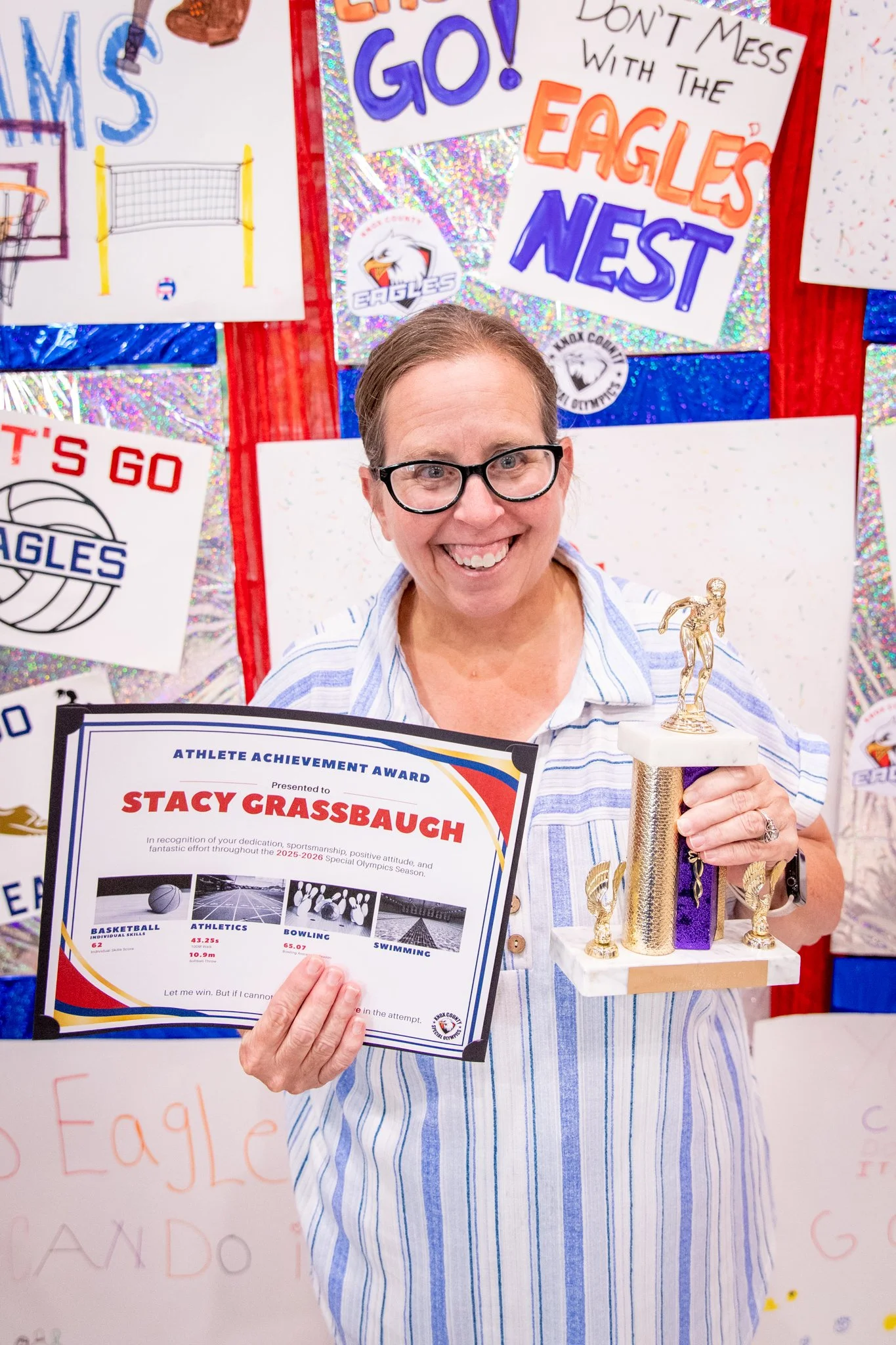 portrait of a person standing in front of a special olympics back drop, holding their trophy and certificate