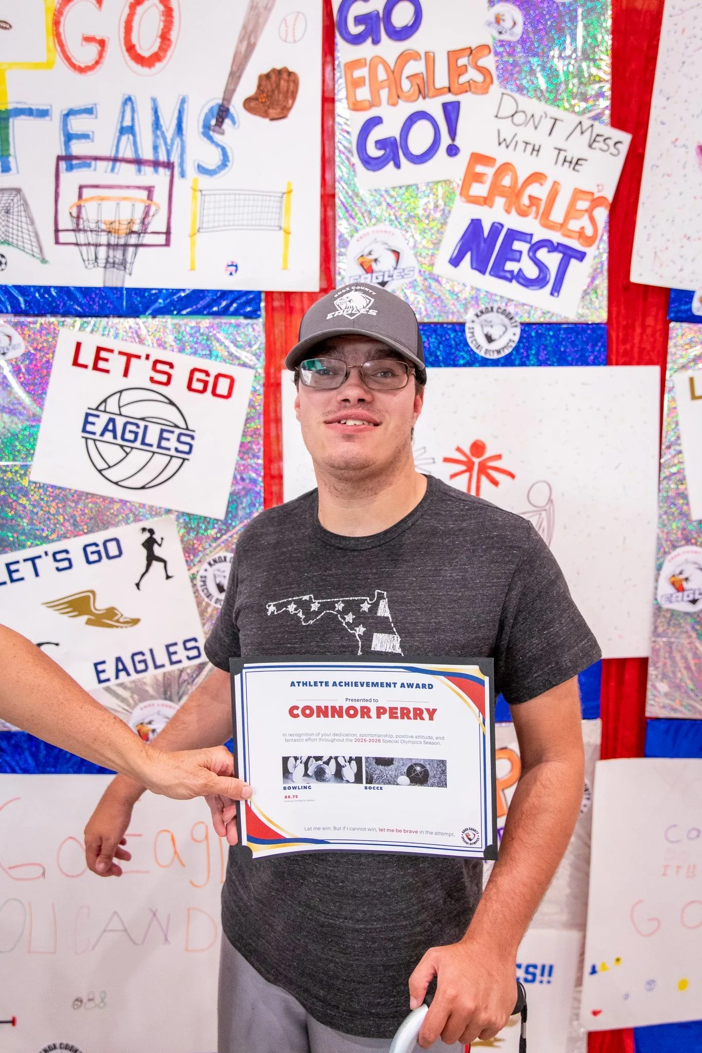portrait of a person standing in front of a special olympics back drop, holding their trophy and certificate