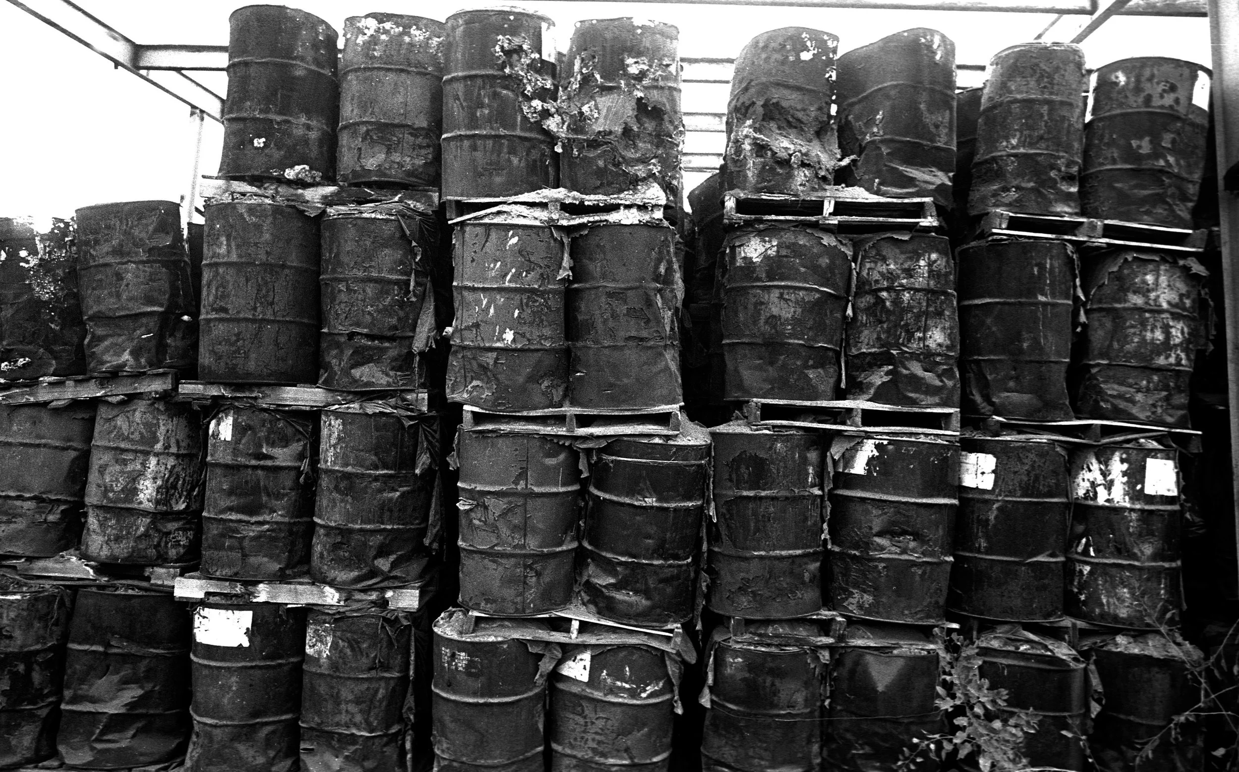 An abandoned battery recycling plant where toxic barrels rot. The 8,500-ton of barrels burst with toxins. Wind carries the waste over the houses below, while rain washes it into a school playground.