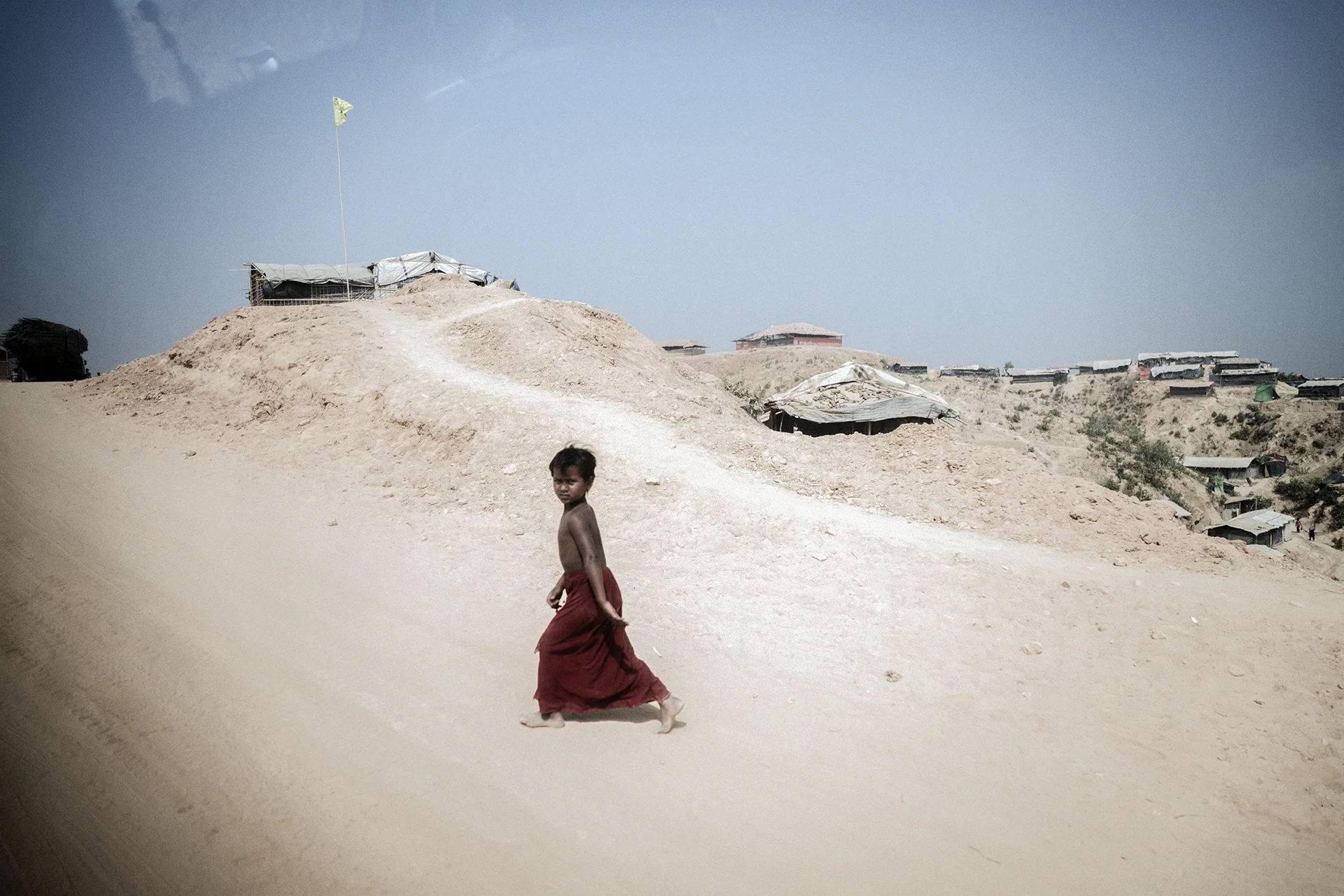 Having been cast into the wilderness after their homes were burnt and their families slaughtered nearly a million Rohingya became refugees in Bangladesh, settling in sprawling camps that they built overnight. This road used to be a rainforest. The rainforest was cut down by the refugees and was transformed into this desert like camp from which are confined to.