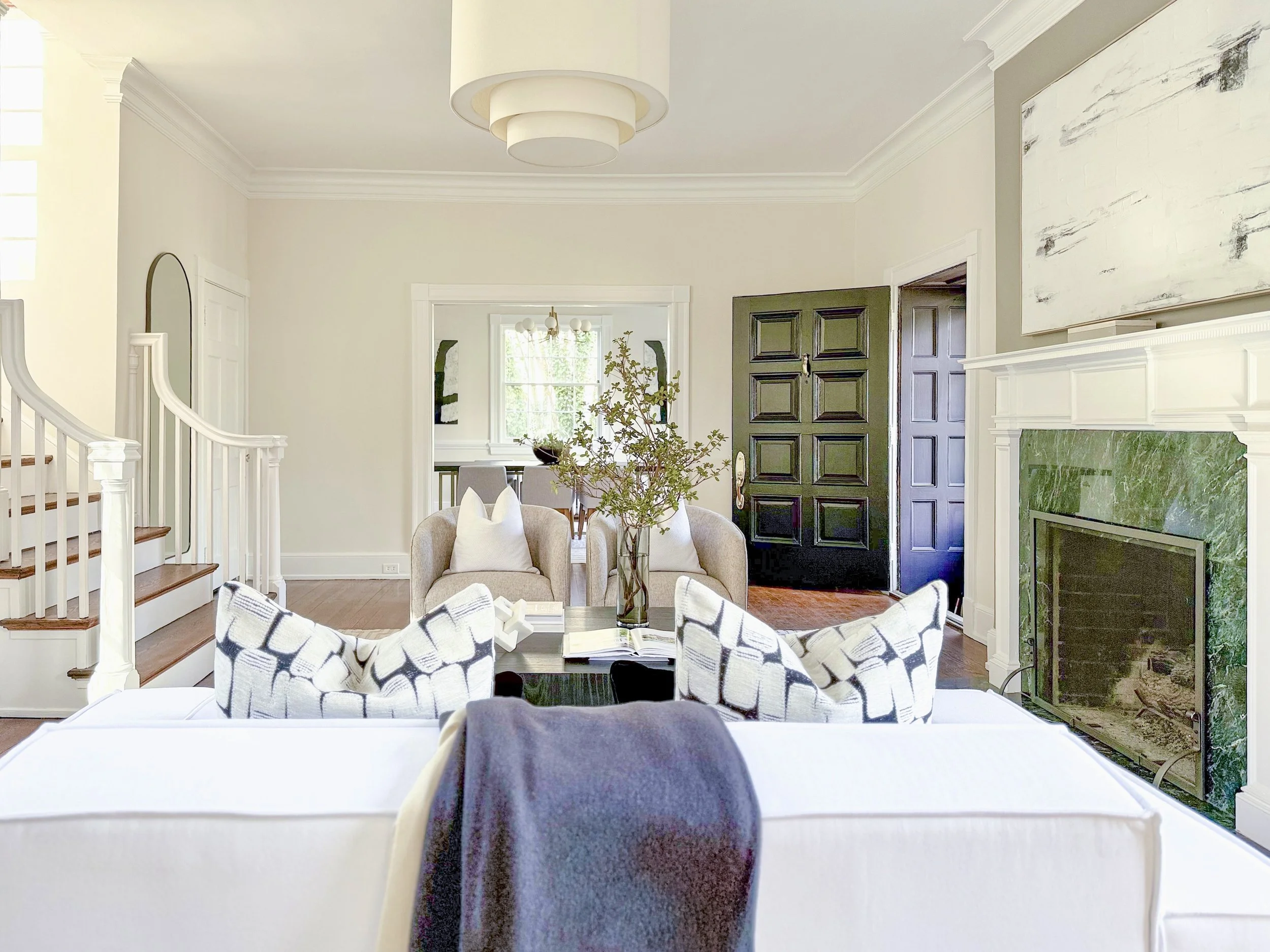 Luxury staged living room in Richmond, VA featuring neutral furnishings, black front doors, green marble fireplace, and bright natural light.