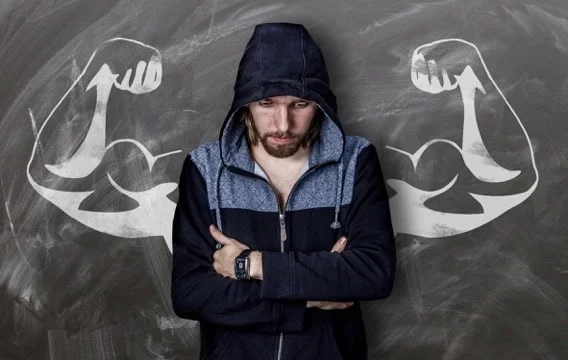 anxious white man with arms akimbo in front of chalkboard with flexing chalk drawn arms