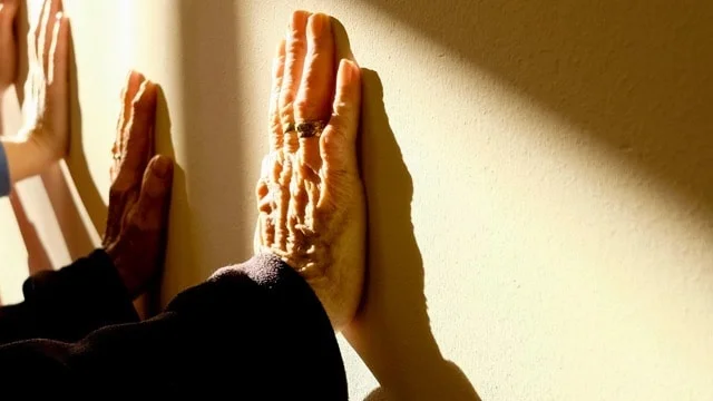 elderly and younger hands pressed against wall