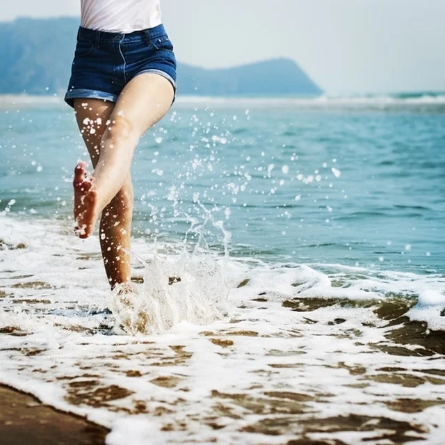 woman kicking up water at the beach