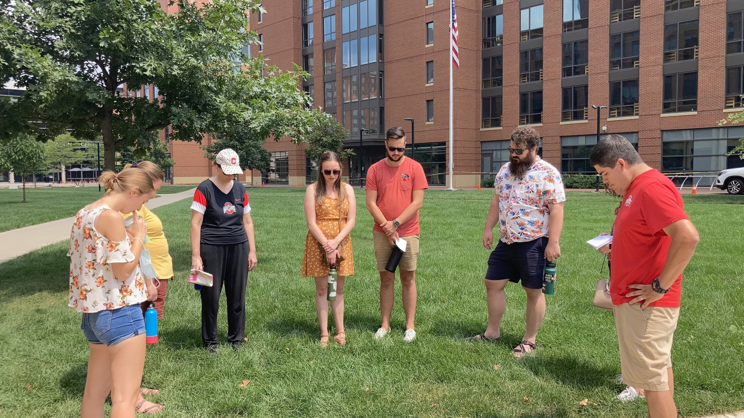 group of people standing in a circle outside on campus, praying