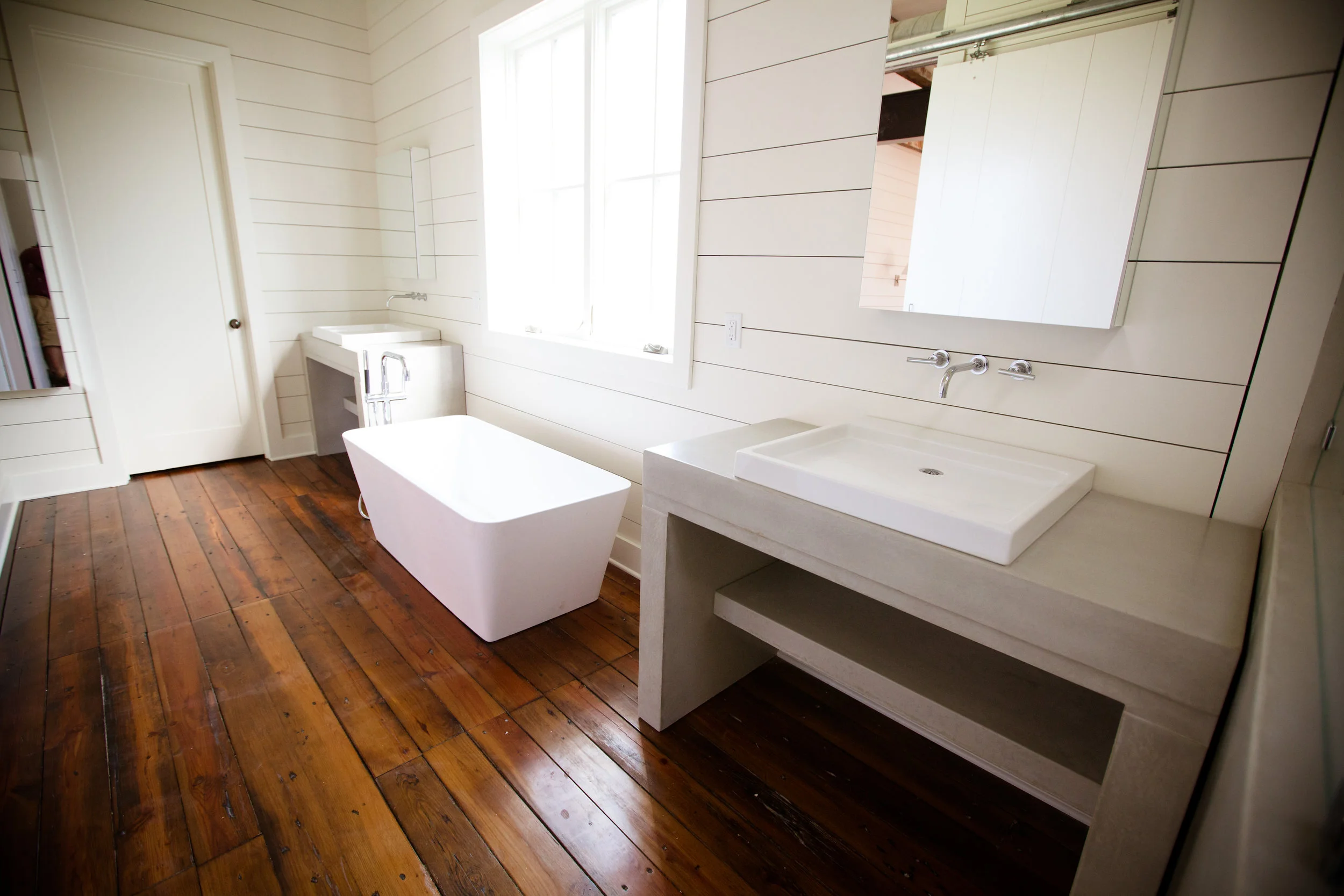 a farmhouse bathroom with concrete vanities and beautiful wood floors