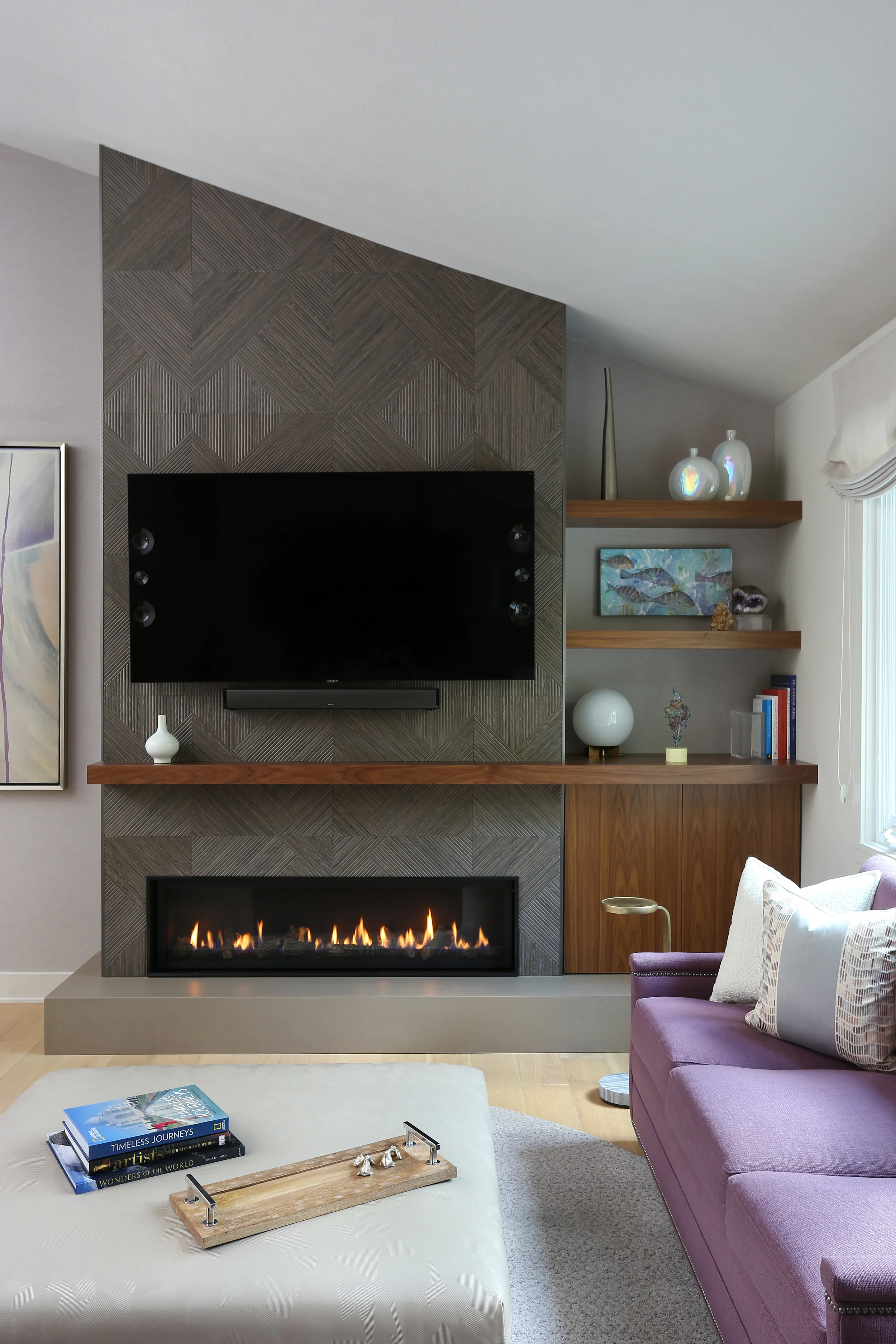 This stunning modern fireplace is truly a focal point. Clad in Porcelanosa geometric tile, the custom walnut millwork and concrete hearth add rich depth to the space. The angles in the ceiling and tile are also subtly repeated in the ottoman vinyl by Kravet. And who doesn't love a purple sofa? 