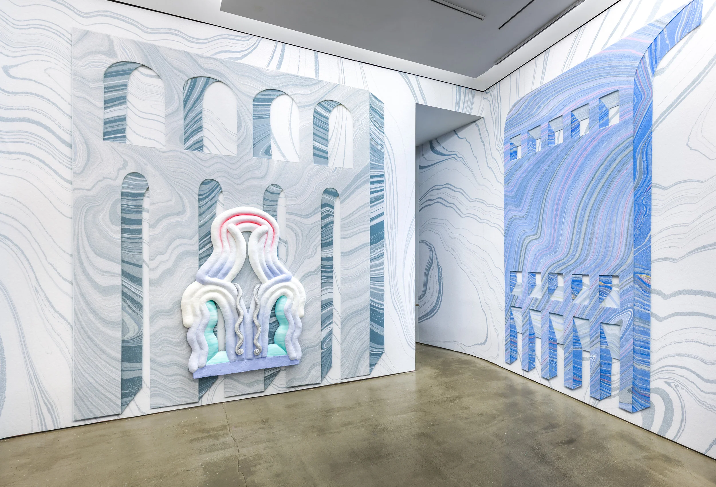 Windows and Walls , 2018 Solo exhibition at Asya Geisberg Gallery, New York, NY Press: Charity Coleman, ArtForum, Critic’s Pick, November 2018 Drew Zeiba, PIN-UP Magazine, January 2019 Steve Rivera, The Great Fires, December 2018 Chloe Valette, Husk Design Blog, November 2018 Art Viewer Asya Geisberg Gallery is pleased to present Lauren Clay, “Windows and Walls”, a solo exhibition of sculpture, mounted on a wallpaper installation that covers the gallery walls. Previously featured in “Monochromatic” at AGG, Clay’s work has become increasingly complex, and in “Windows and Walls” the marbleized wallpaper and biomorphic sculpture intertwine visually and conceptually. Originating as white, textured twists on the angular rigidity and slickness of Minimalism, Clay’s sculptures adopt pronounced references to space, architecture, and the body, and add high color and detailed curlicues. In tandem, her wallpaper acquires a double layer of illusionistic yet improbable spaces floating on a background of seemingly never-ending undulating stripes of color. The artist’s process translates a small collage of hand-marbled paper into an immersive floor-to-ceiling environment. Using traditional marbling techniques that evoke antique books, Clay’s psychedelic patterns leap from elegant old-world decoration to contemporary, digitally scanned, and aggressively scaled work. In this exhibition, a riddle of Escher-like patterns with quixotic spaces forms a backdrop for equally playful sculptures, which similarly vibrate between flat and illusionistic space. The viewer is asked to re-situate oneself continually – the sculptures fold and curve in rhythmic parallels, but also interrupt the gaze with cracks of bright color, and suggest openings or windows that force a point of view. In Clay’s universe, instead of a window into real space the negative spaces act as a frame for the wallpaper, frustrating the need for “here” and “there”. The sculptures hint at the physicality suggested by the wallpaper, whose architectural arches, columns, and possible edifices are nonetheless patently unreal. The ever more oneiric spaces - influenced by the architecture of Claude Costy, Le Corbusier, Aldo Rossi, or the drawings of Nathalie du Pasquier – turn the gallery into pathways through time, space, and scale. The sculptures suggest orifices, dangling limbs, or undulating anemones, with colored details that could be petals, tongues, or wrought iron accents. Gravity of curvy flesh is felt, but so paradoxically is the rigidity of carved steps or medieval arrow-slit windows. Clay makes sure that we keenly sense the authority of the artist’s hand, whether in the roughly-grooved sculptures or the painterly poetics of pigment floating through water. The very idea of marbling – suggesting a stone’s striations via drops of paint on barely-there paper – shows the interplay inherent in Clay’s entire project – combining painting, sculpture, architecture, and design to re-envision their potential for spatial contrast, fantasy, and confusion.